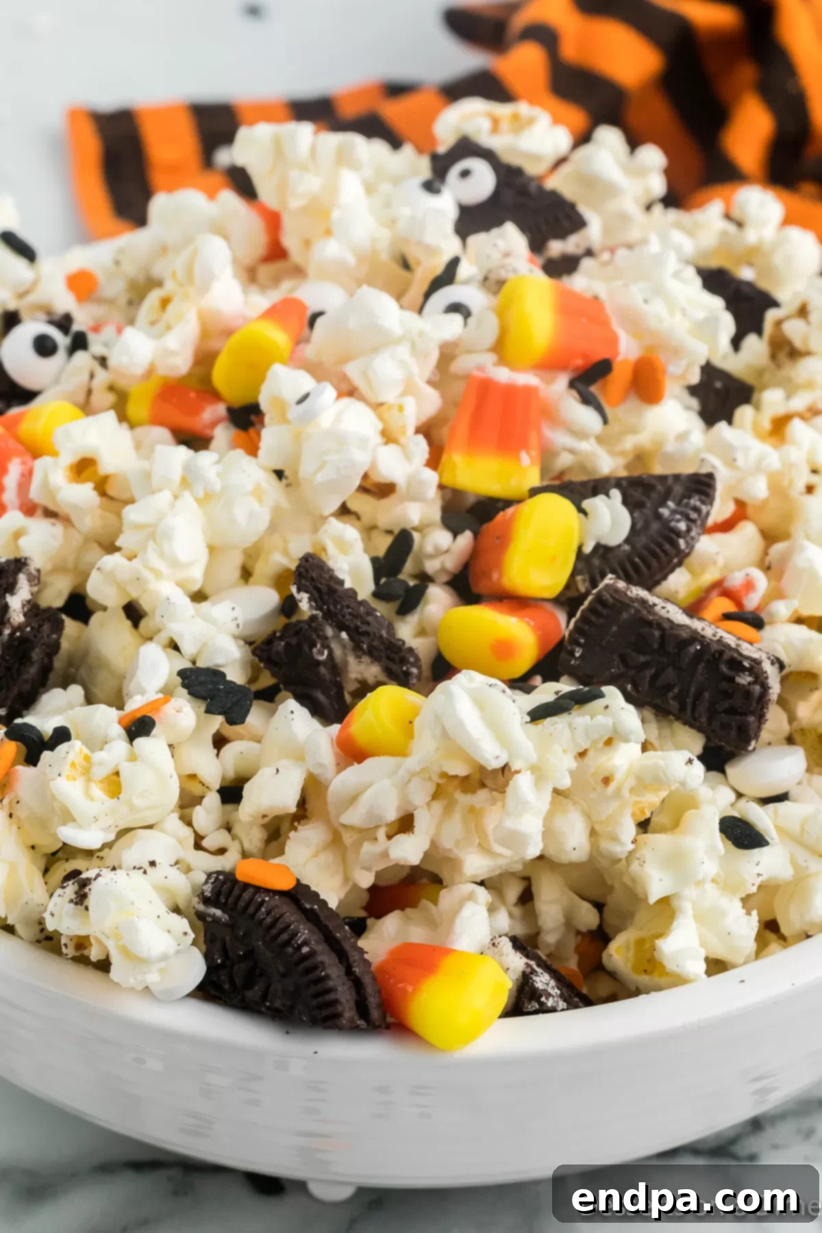 Haunted Kernels 8 A large bowl filled with festive Halloween Popcorn, showcasing the colorful candy corn, dark Oreos, and whimsical candy eyes against the white chocolate coating.