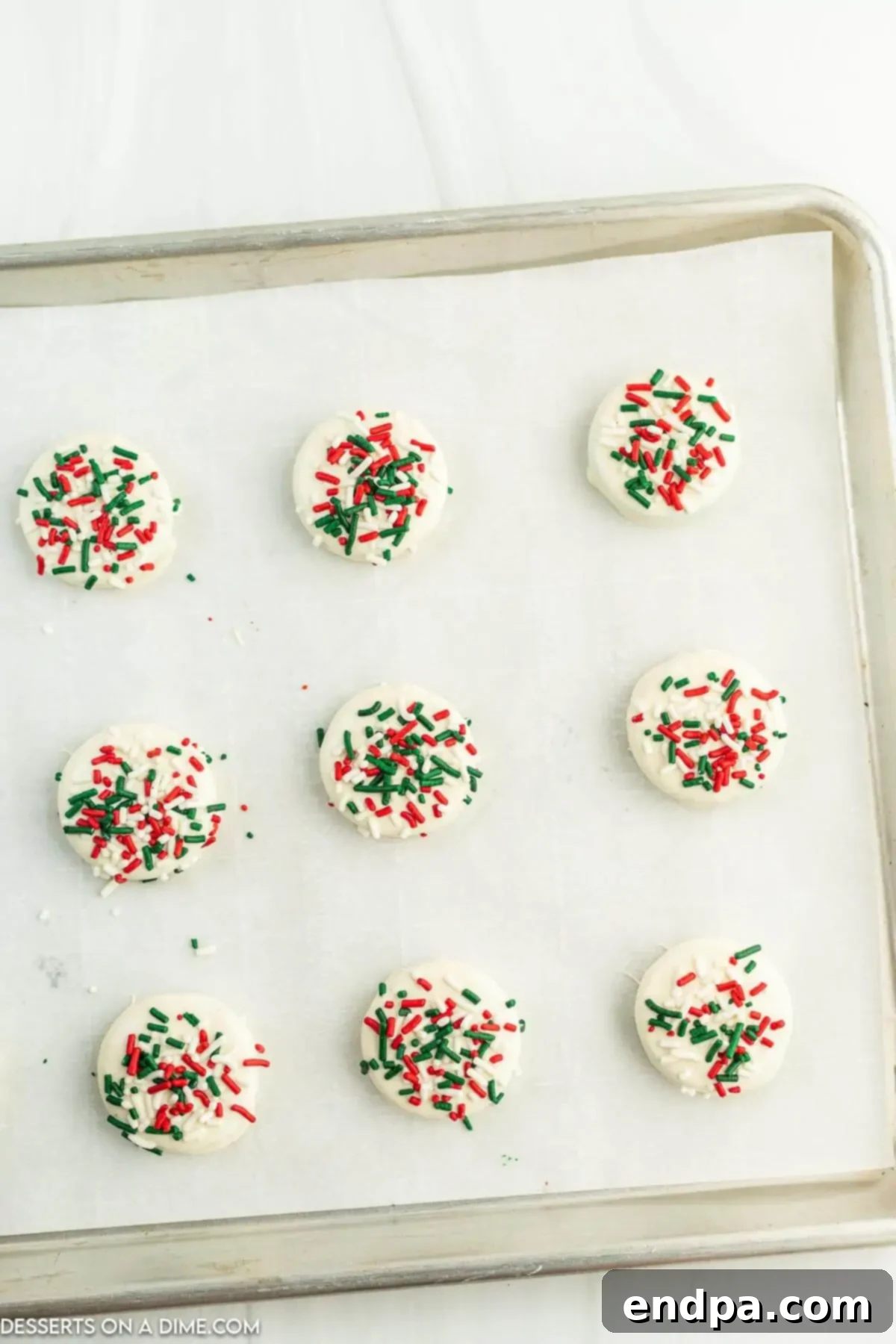 Holiday Oreo Delights 6 White chocolate coated Oreo cookies on parchment paper, topped with festive Christmas sprinkles.