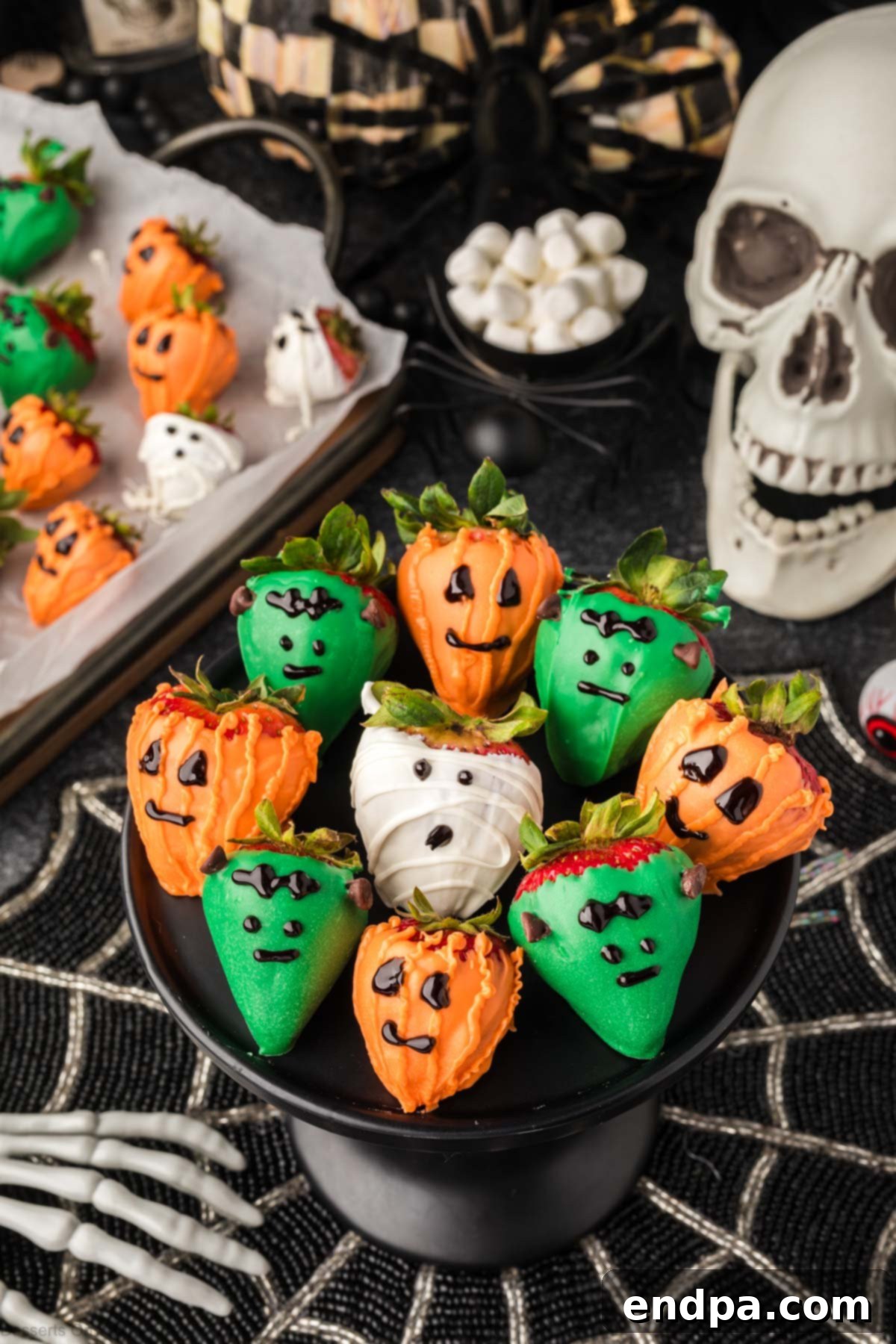 A black platter filled with various Halloween chocolate covered strawberries, including ghost, pumpkin, and Frankenstein designs.