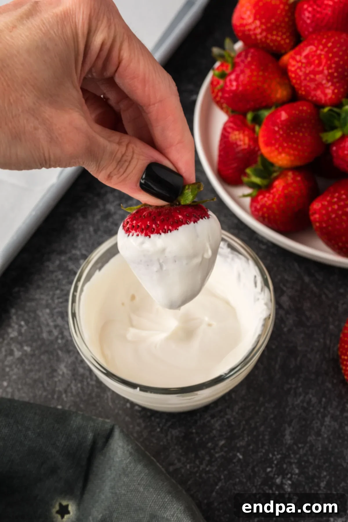 A strawberry being dipped into melted white candy wafers, covering it completely.
