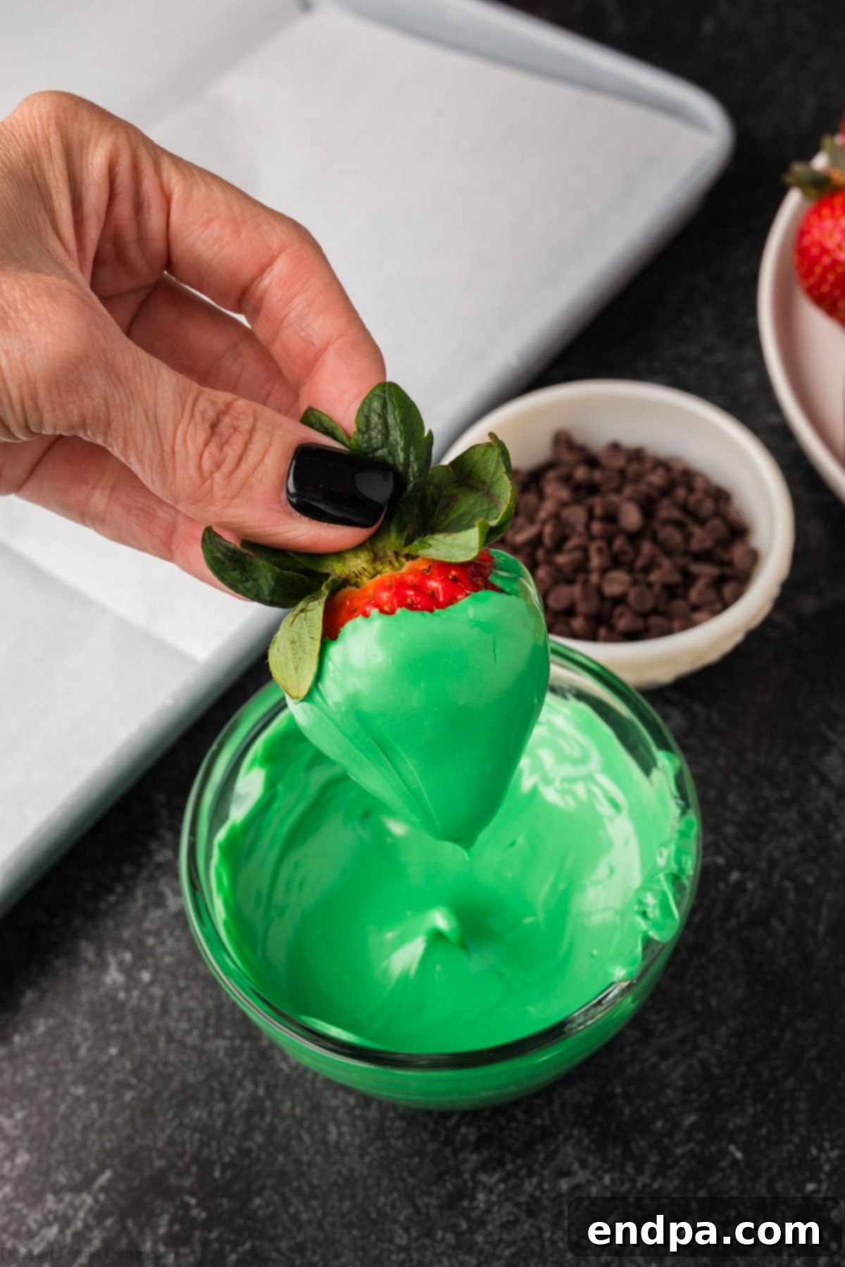 A strawberry dipped in melted green candy wafers, ready to be transformed into Frankenstein.