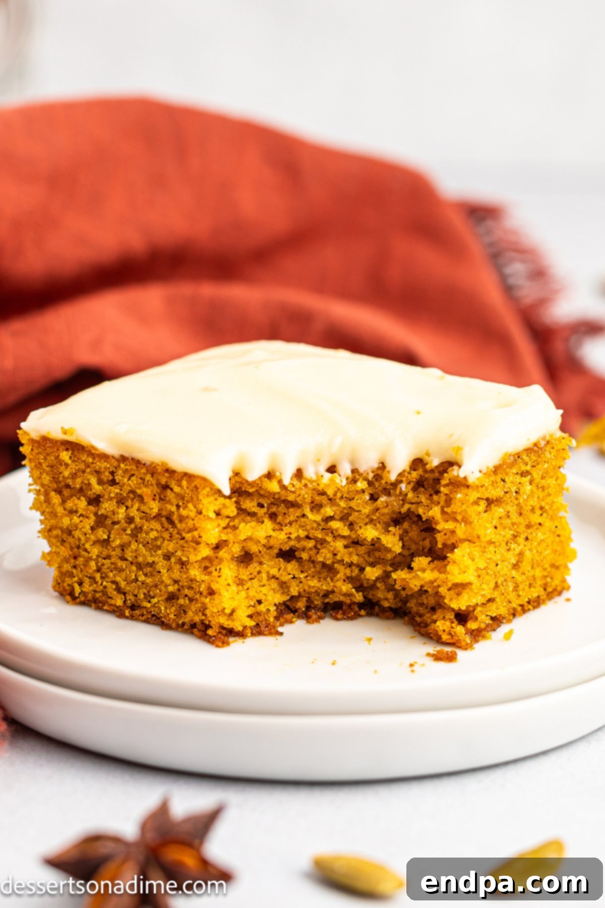A slice of moist pumpkin sheet cake with thick cream cheese frosting on a white plate, garnished with a sprinkle of cinnamon.