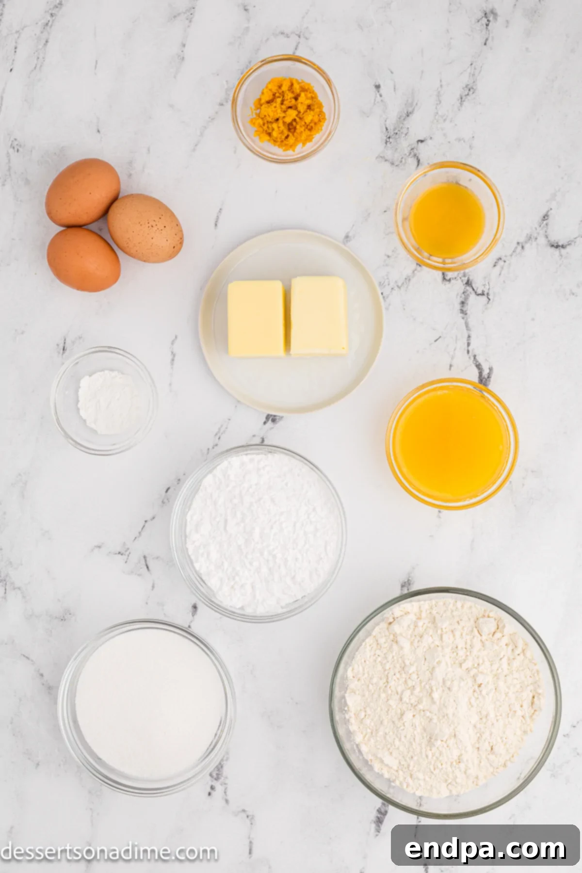 A flat lay of all the ingredients for orange pound cake, including flour, eggs, sugar, butter, oranges, and powdered sugar, arranged on a white background.