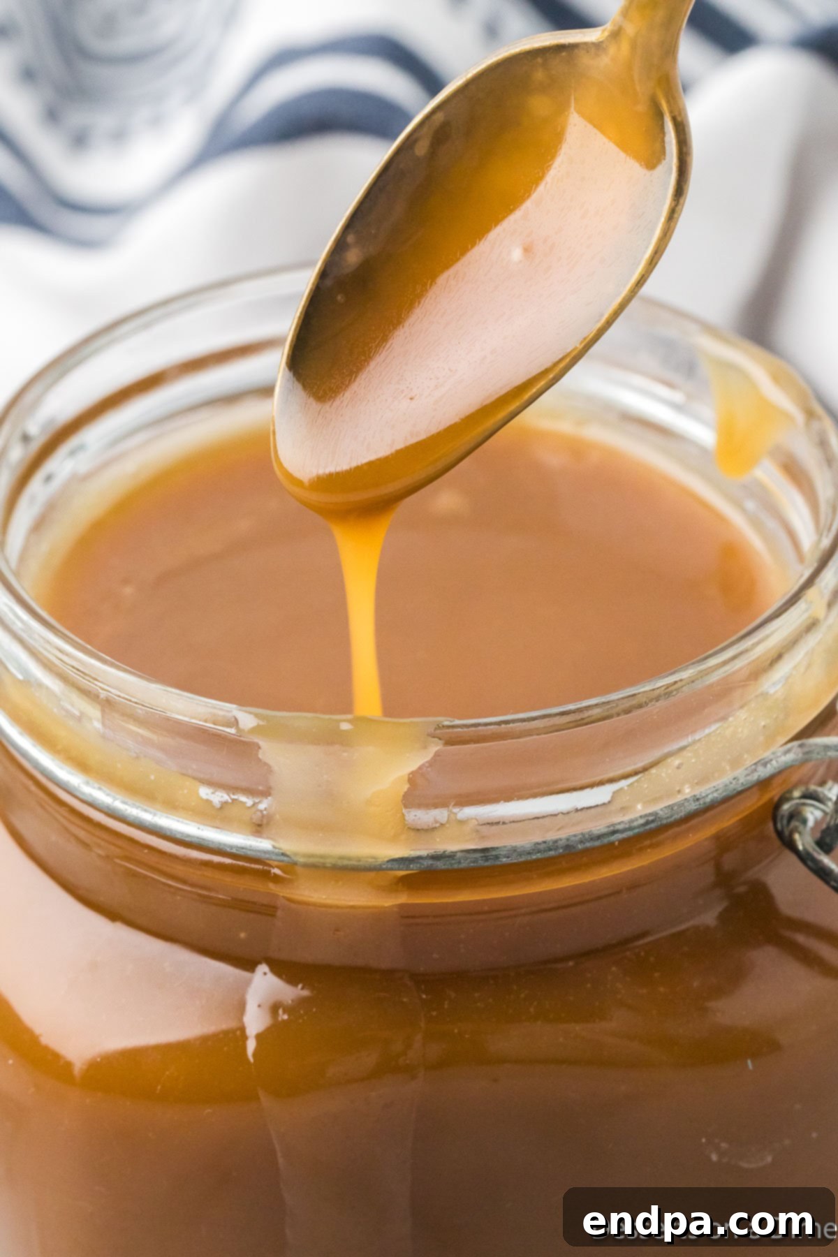 Decadent Homemade Caramel 2 A beautiful glass jar filled with luscious homemade caramel sauce, with a spoon resting elegantly, ready to be enjoyed.