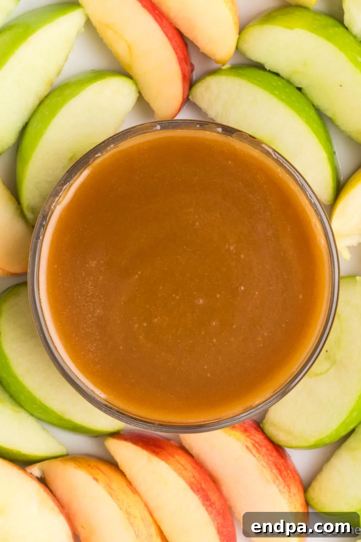 Decadent Homemade Caramel 6 A bowl of homemade caramel sauce surrounded by fresh apple slices, perfect for dipping.