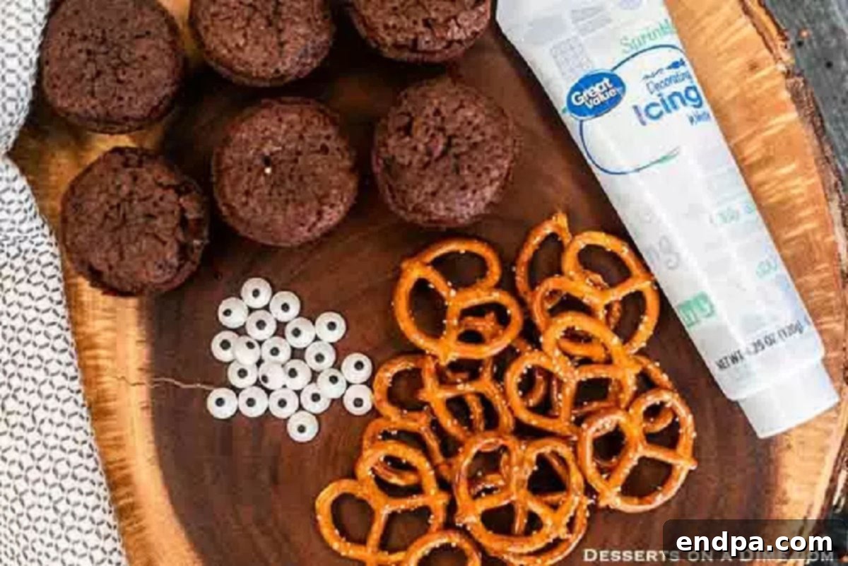Ingredients for Easy Spider Brownies: A flat lay showing mini brownies, pretzel twists for legs, white frosting for adhesion, and colorful candy eyes for decoration.