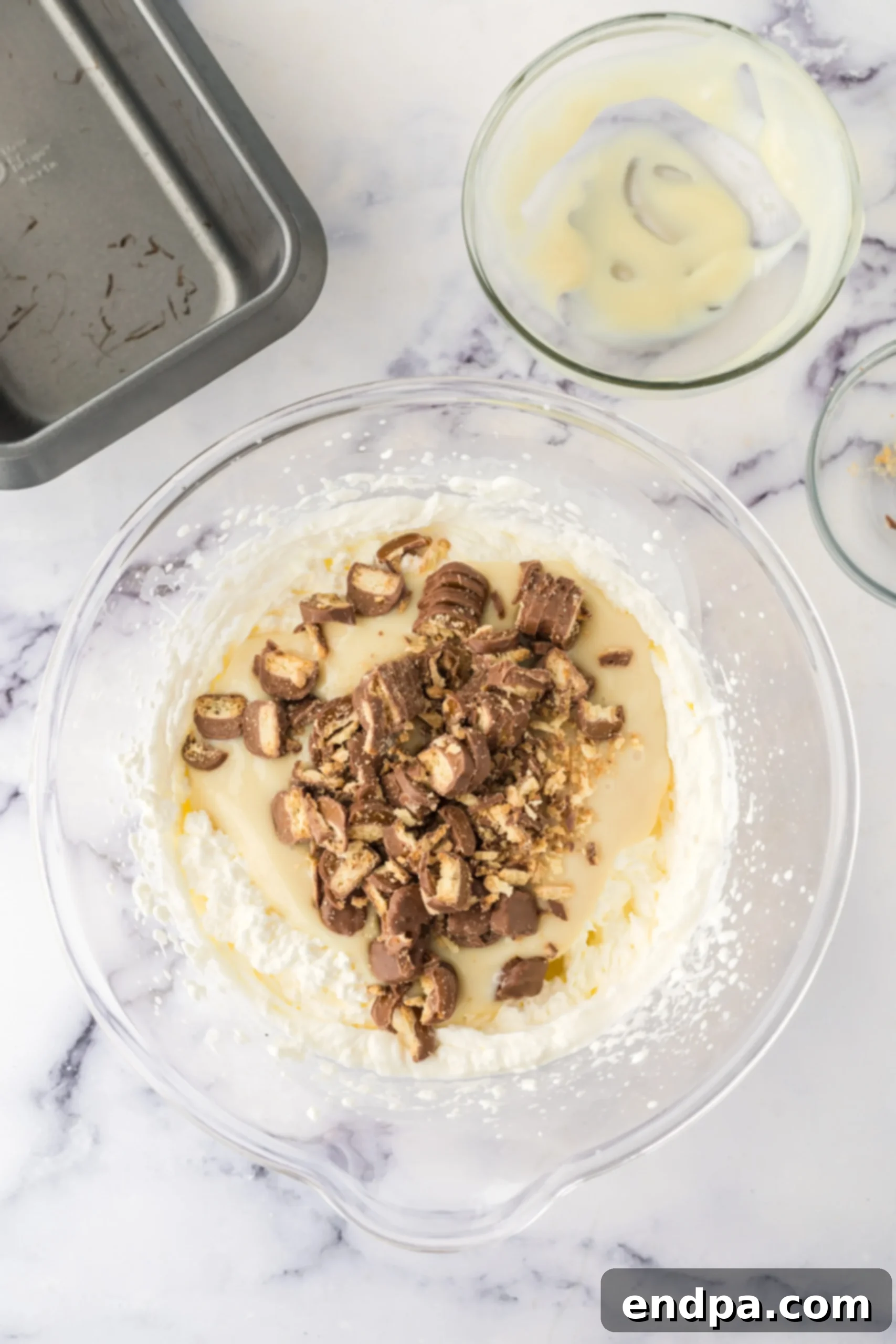 Folding sweetened condensed milk and chopped Twix candy bars into whipped cream.