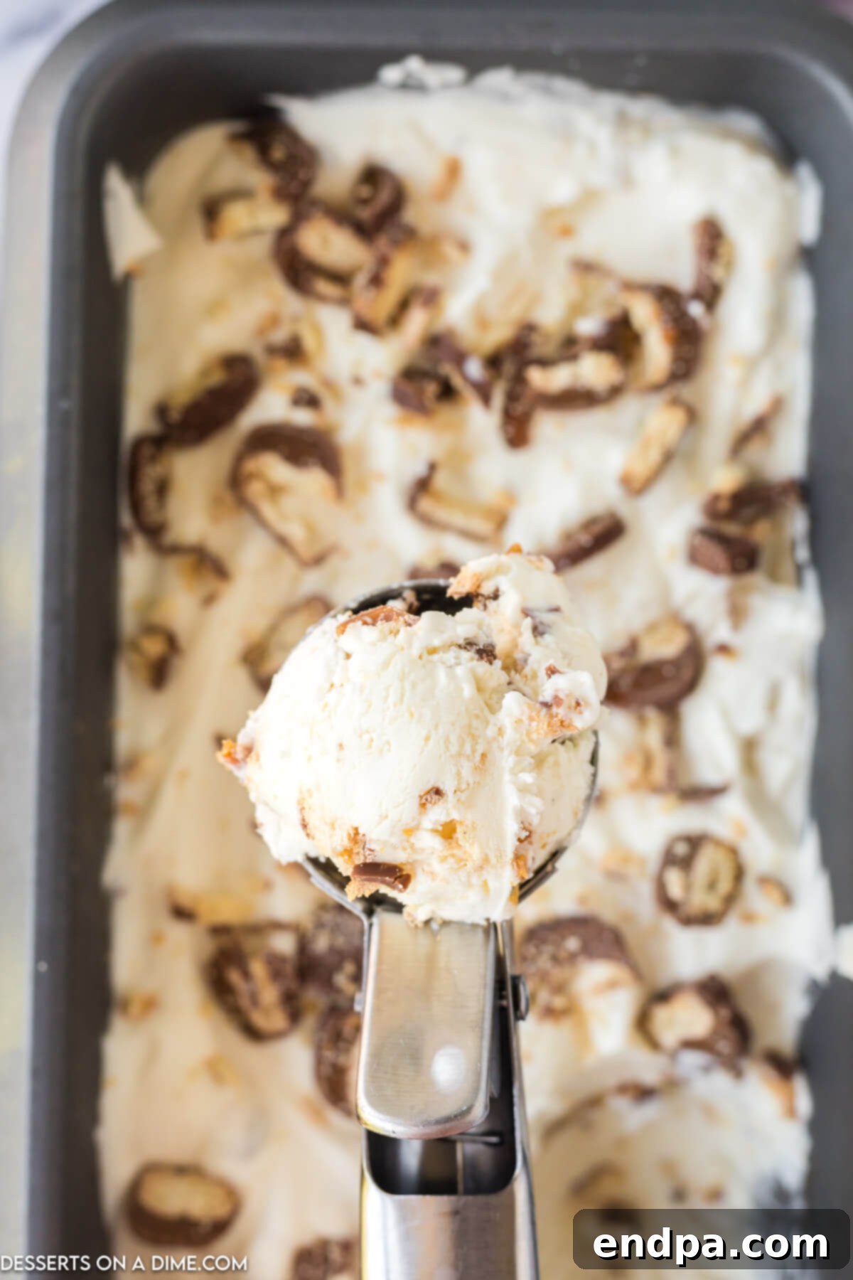 Scooping frozen Twix ice cream from a loaf pan.