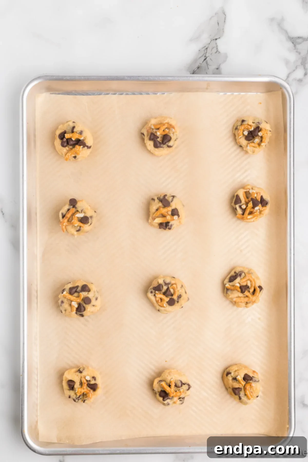 Cookie dough balls gently pressed down and topped with additional chocolate chips and crushed pretzel pieces.