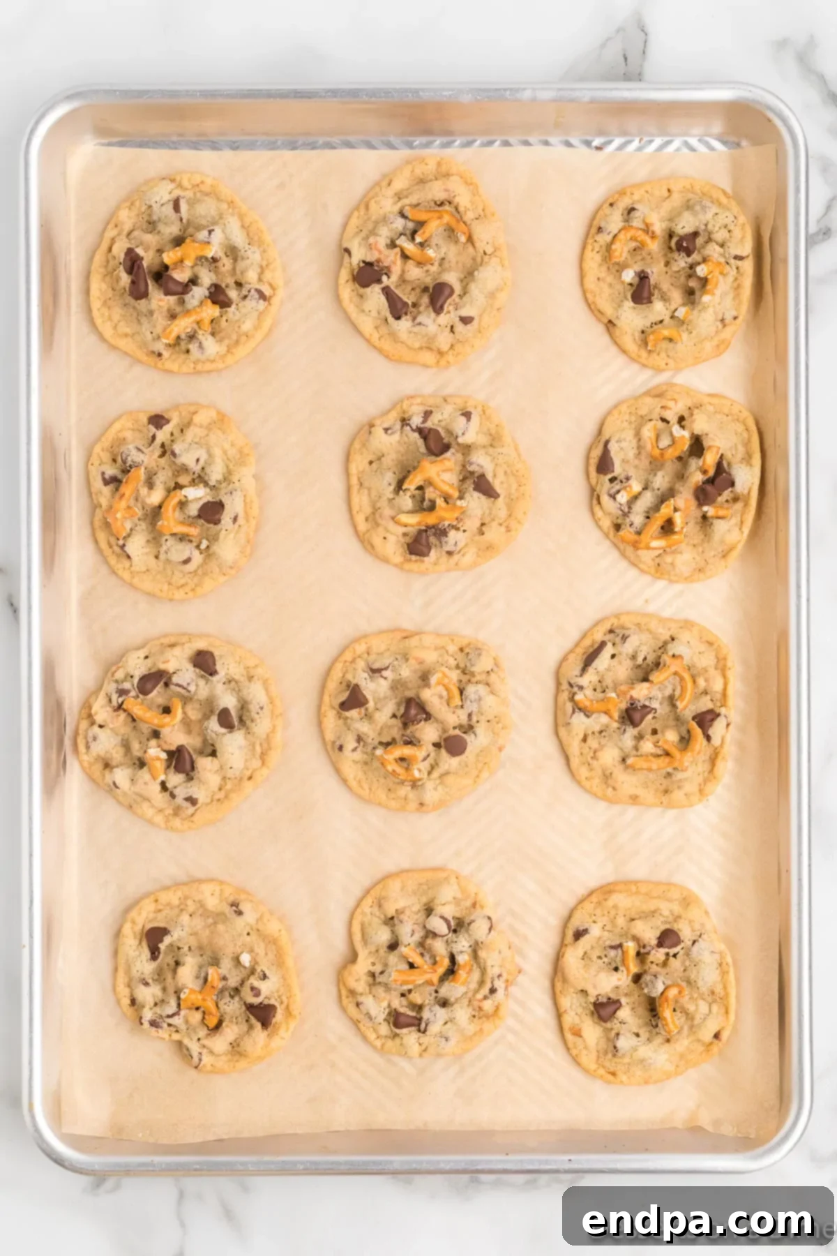 Freshly baked Chocolate Chip Pretzel Cookies still on the baking sheet, with slightly golden brown edges.