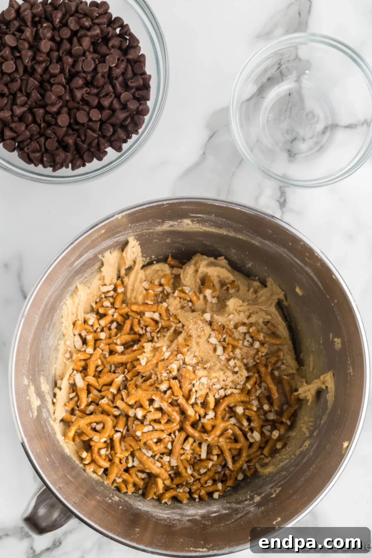 Crushed pretzel pieces and chocolate chips being gently folded into the cookie dough by hand.