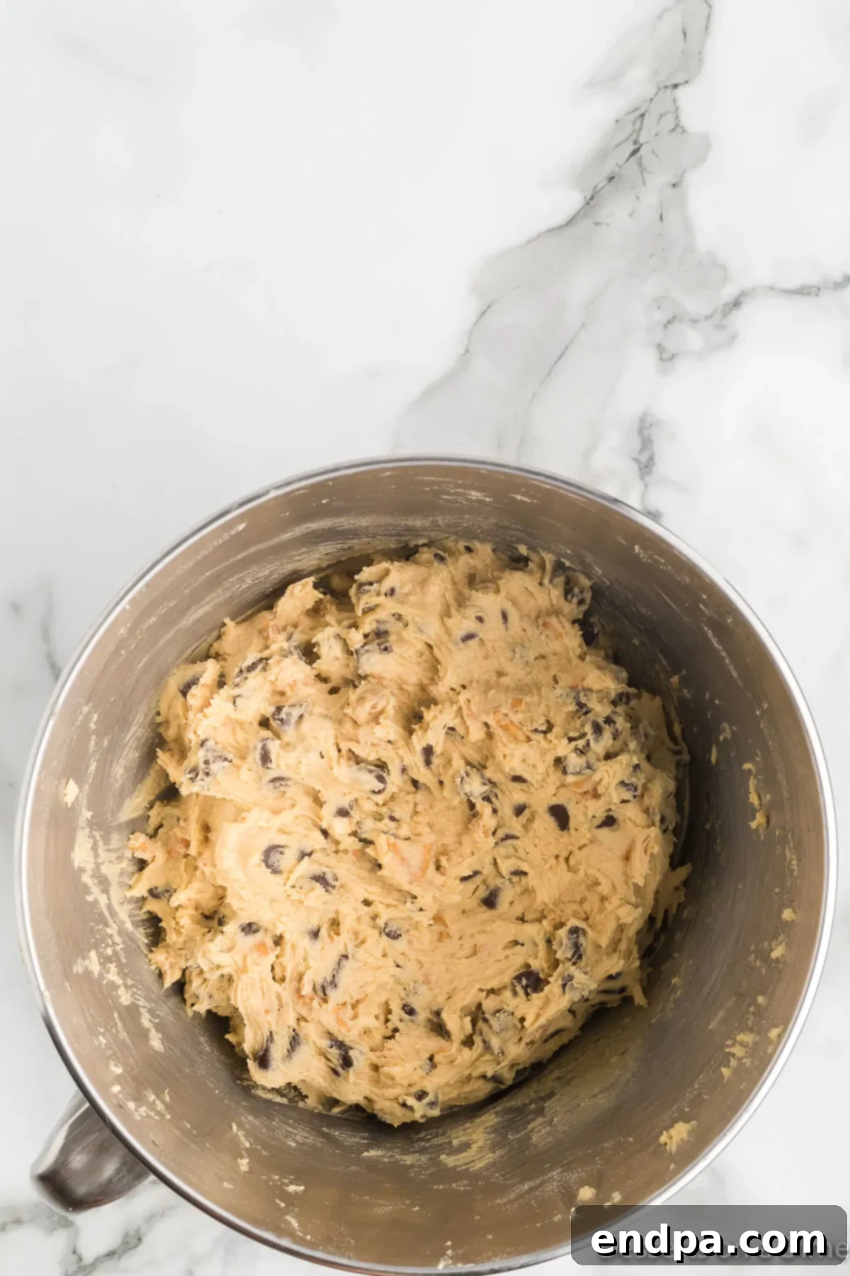 Cookie dough, now with pretzels and chocolate chips, in a bowl and covered, ready for chilling.