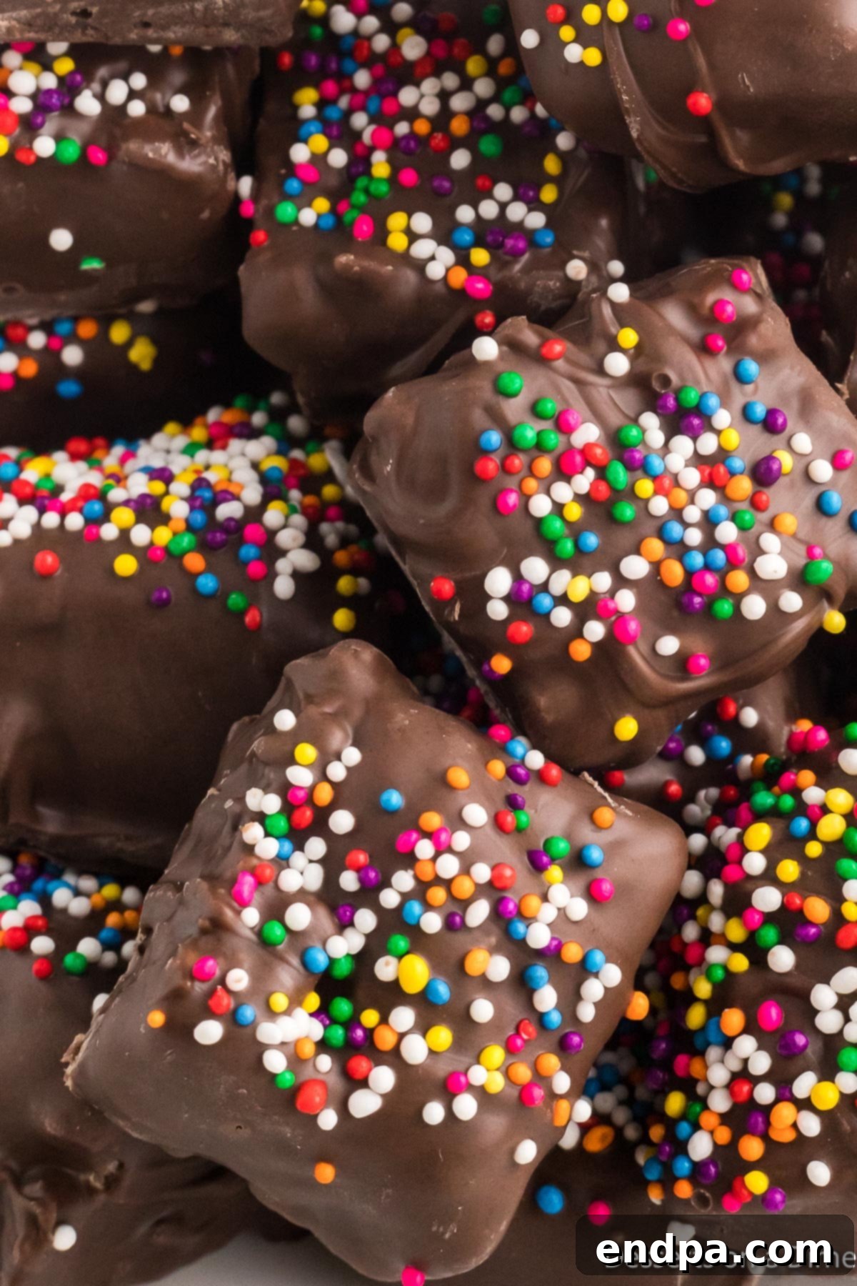 A tempting pile of Chocolate Covered Rice Krispie Treats, each piece glistening with chocolate and colorful sprinkles.