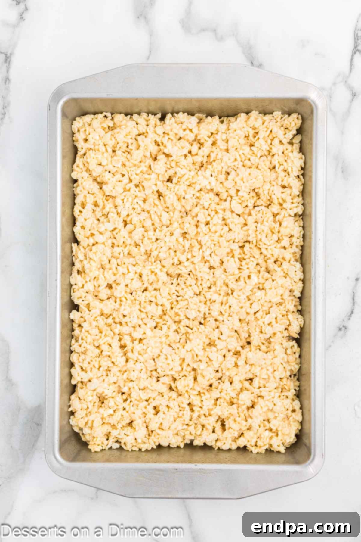 The marshmallow and cereal mixture being gently pressed into a baking pan.