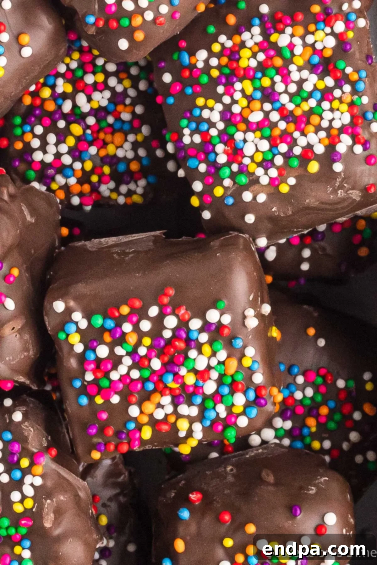 A close-up shot of several Chocolate Covered Rice Krispie Treats piled together, showcasing their chocolate coating and colorful sprinkles.