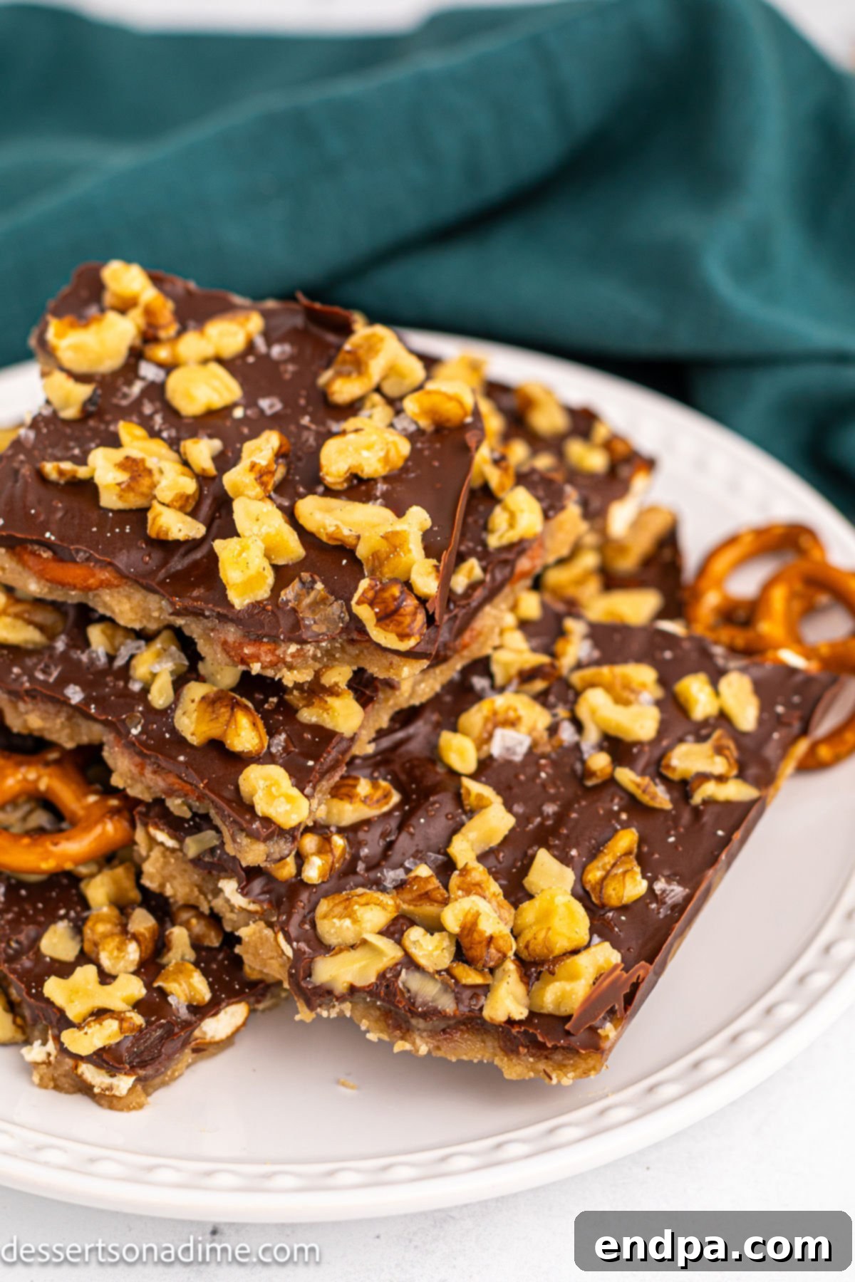 Twisted Toffee Treat 2 Pretzel Toffee broken into irregular pieces on a rustic white plate, garnished with a sprinkle of sea salt.