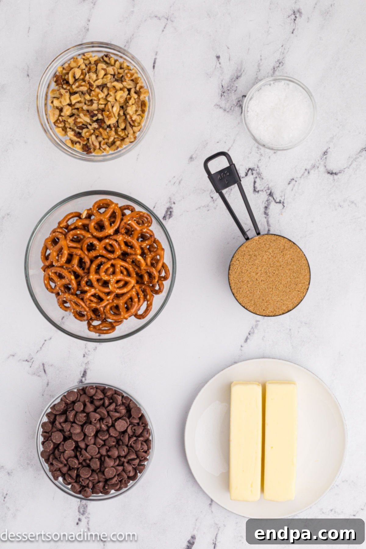 Twisted Toffee Treat 3 Ingredients for pretzel toffee laid out: mini pretzels, sticks of butter, brown sugar, chocolate chips, walnuts, and a small dish of sea salt.