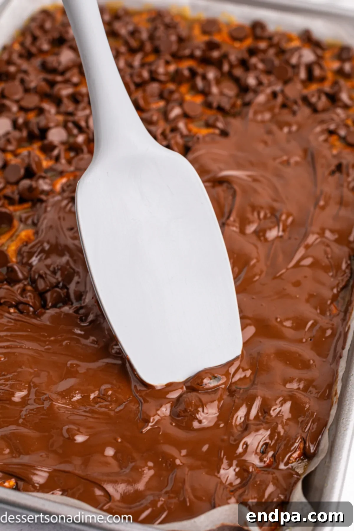Twisted Toffee Treat 10 Melted chocolate being smoothly spread over the pretzel and toffee base using a spatula.