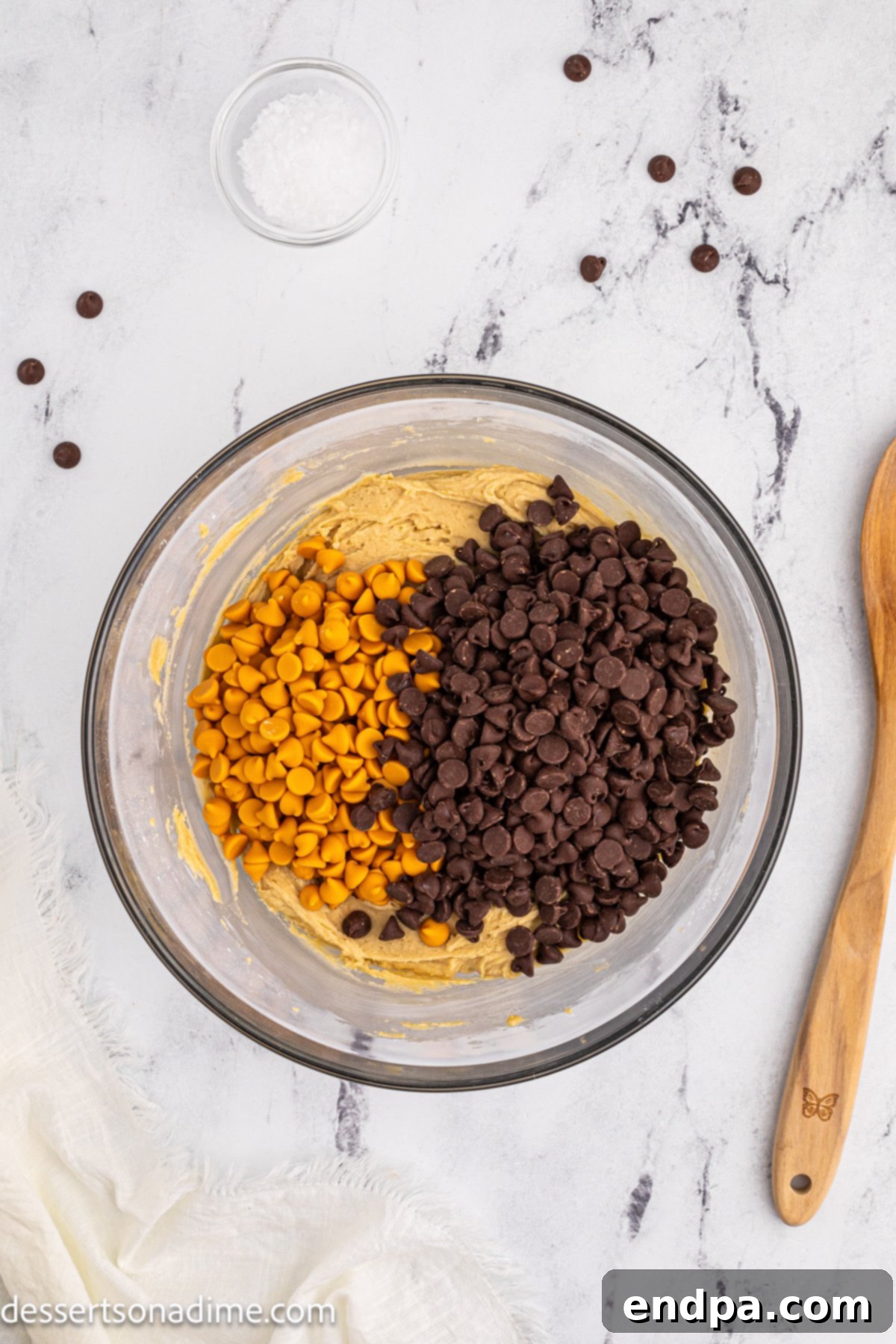 Butterscotch chips and chocolate chips generously scattered over the prepared cookie dough in a bowl.