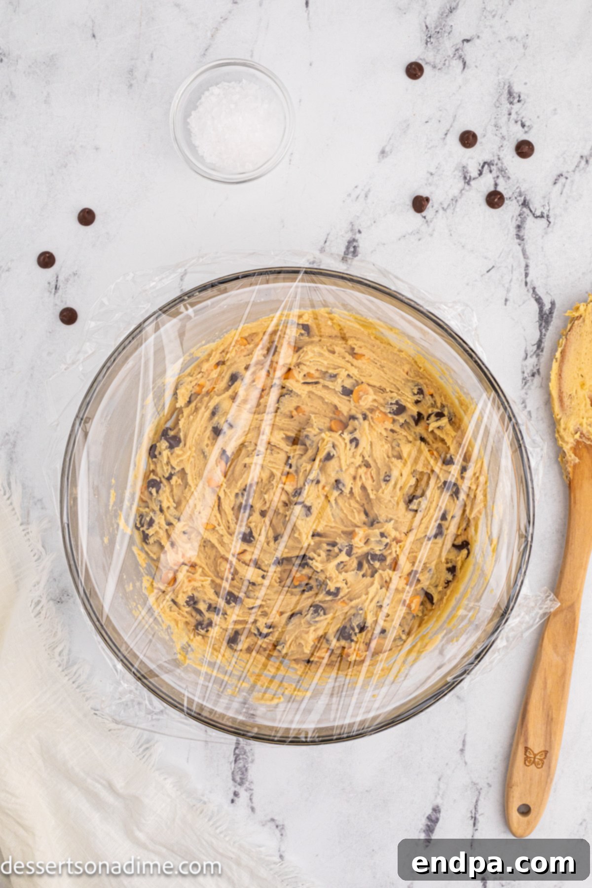 A bowl of cookie dough covered with plastic wrap, chilling in the refrigerator.