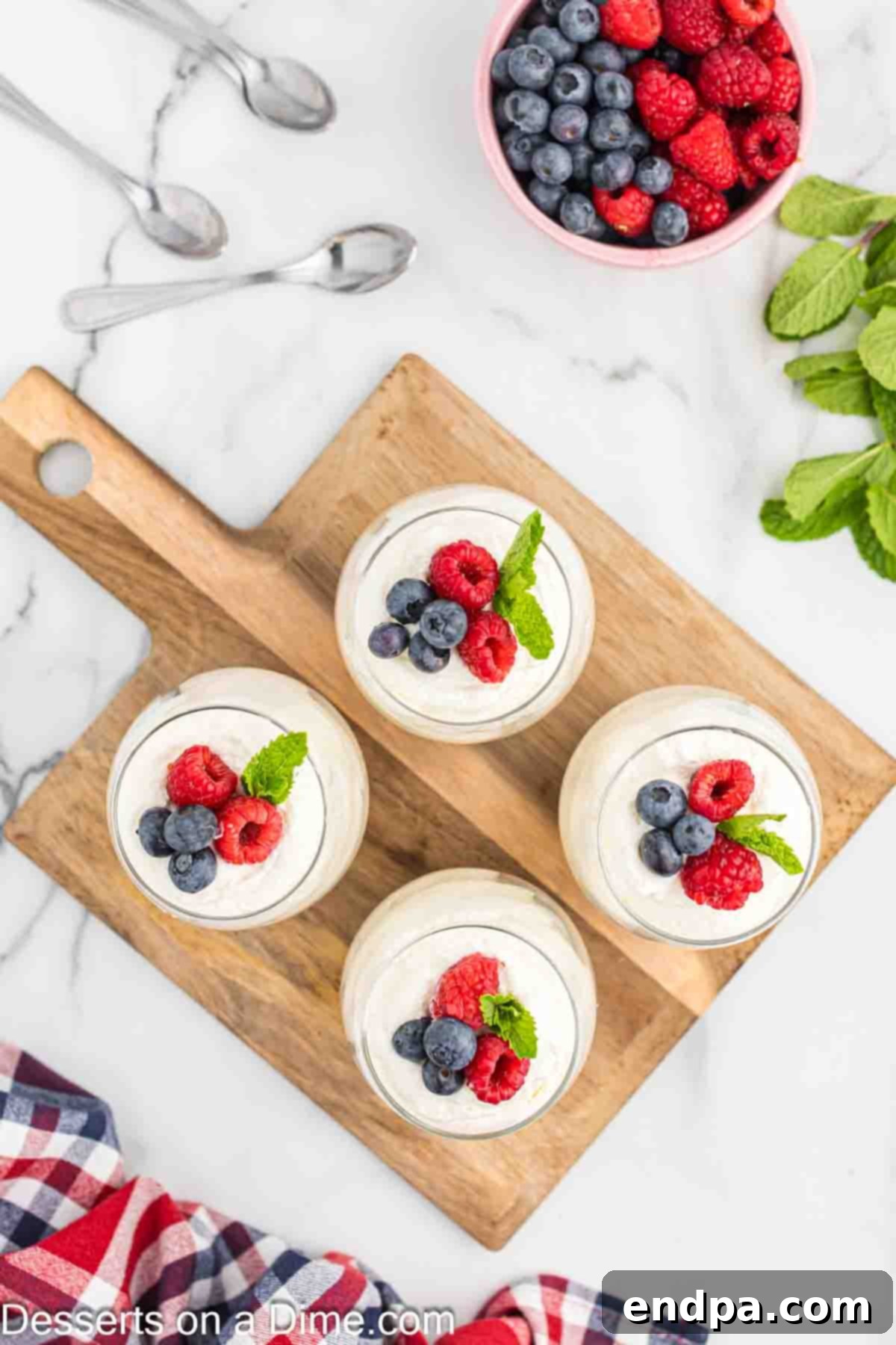 Finished cheesecake mousse cups, each garnished with fresh berries and a small sprig of fresh mint.