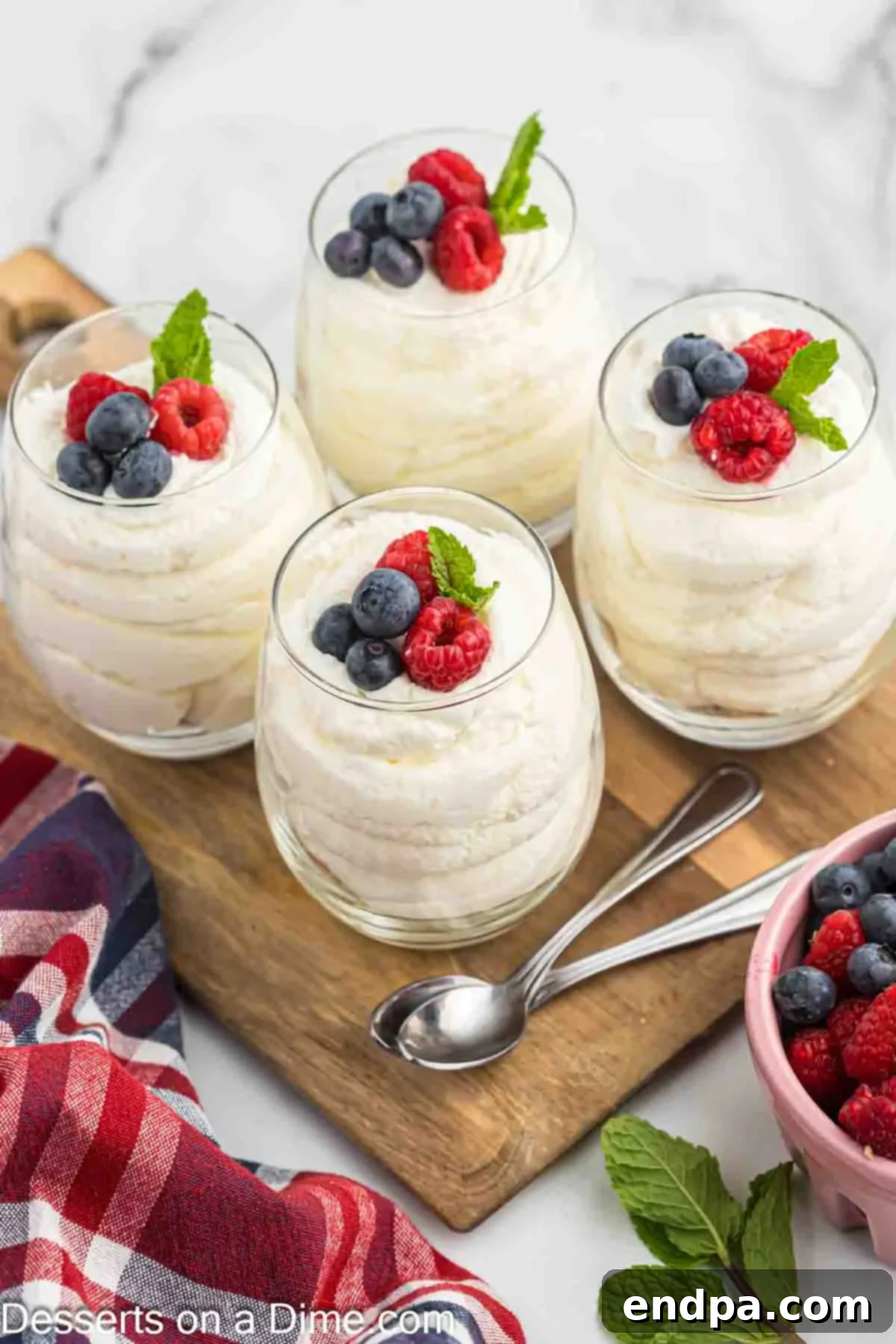 A close-up view of a glass filled with cheesecake mousse, topped generously with fresh blueberries, raspberries, and a delicate mint leaf, ready to be enjoyed.