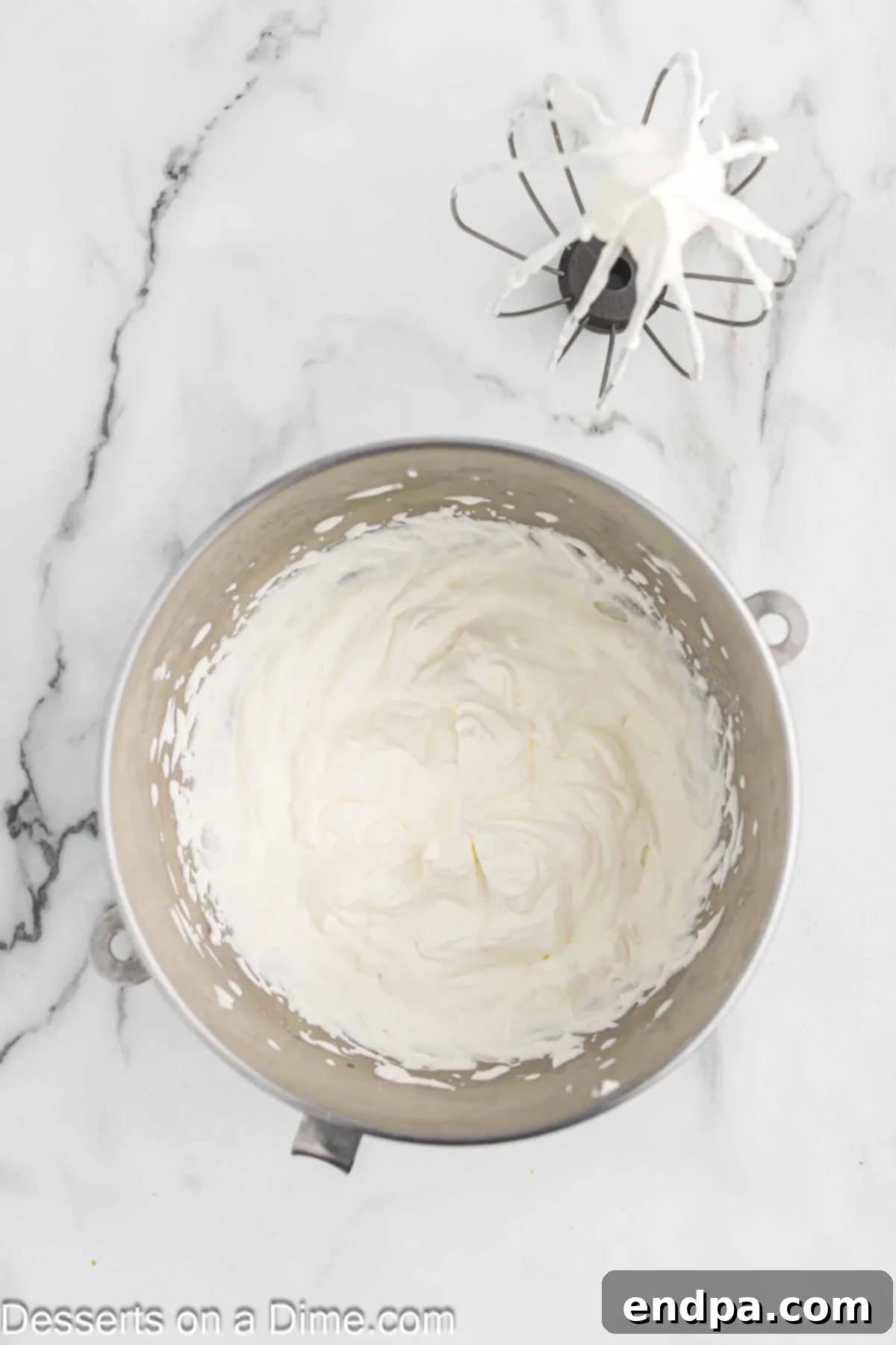 Heavy cream being whipped to soft peaks in a large mixing bowl using a stand mixer with a whisk attachment.