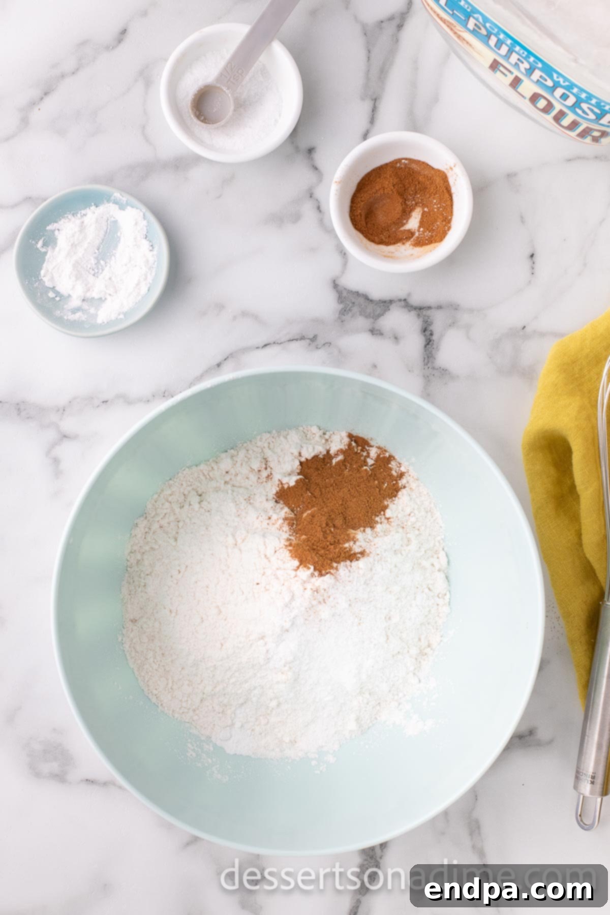 A mixing bowl containing dry ingredients: flour, baking powder, cinnamon, and salt, whisked together.