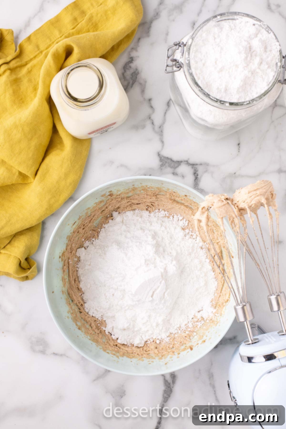 Powdered sugar being gradually added to the butter, brown sugar, and vanilla mixture for frosting.