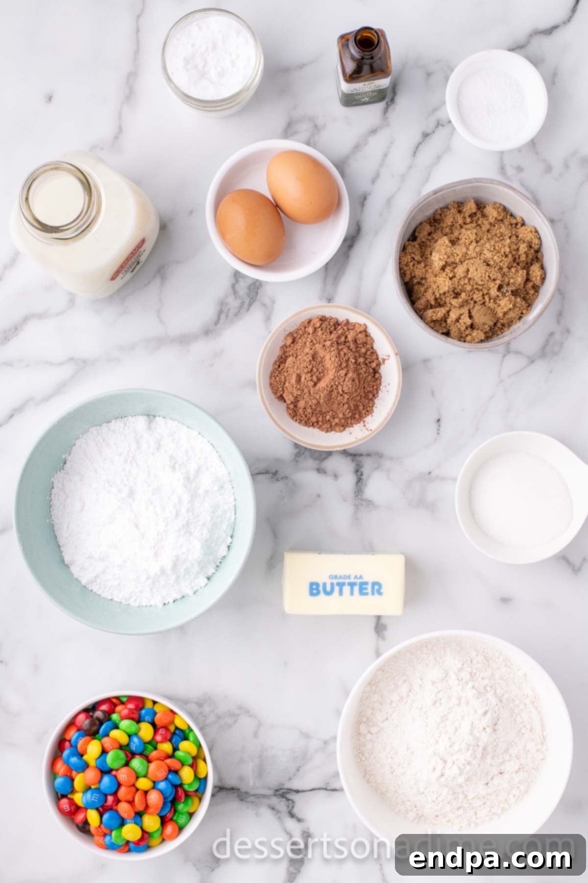 Ingredients for M&M cookie cake - butter, brown sugar, granulated sugar, eggs, vanilla, M&Ms, cocoa powder, butter.