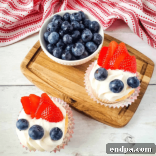 Patriotic Red, White, and Blue Angel Food Cake Cupcakes topped with white frosting and fresh berries.