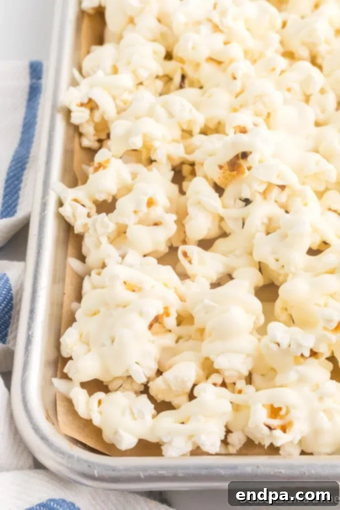 Popcorn spread on a baking sheet, generously coated with melted white chocolate, before it hardens.