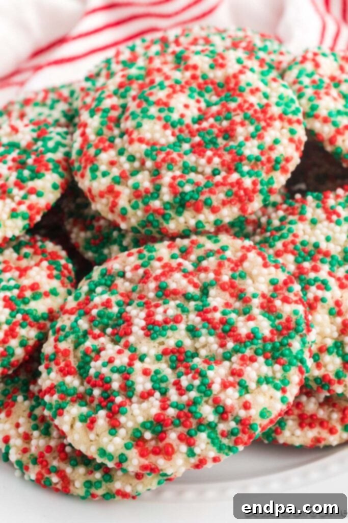 Stack of freshly baked Christmas sprinkle cookies, adorned with red, green, and white sprinkles, on a festive background.