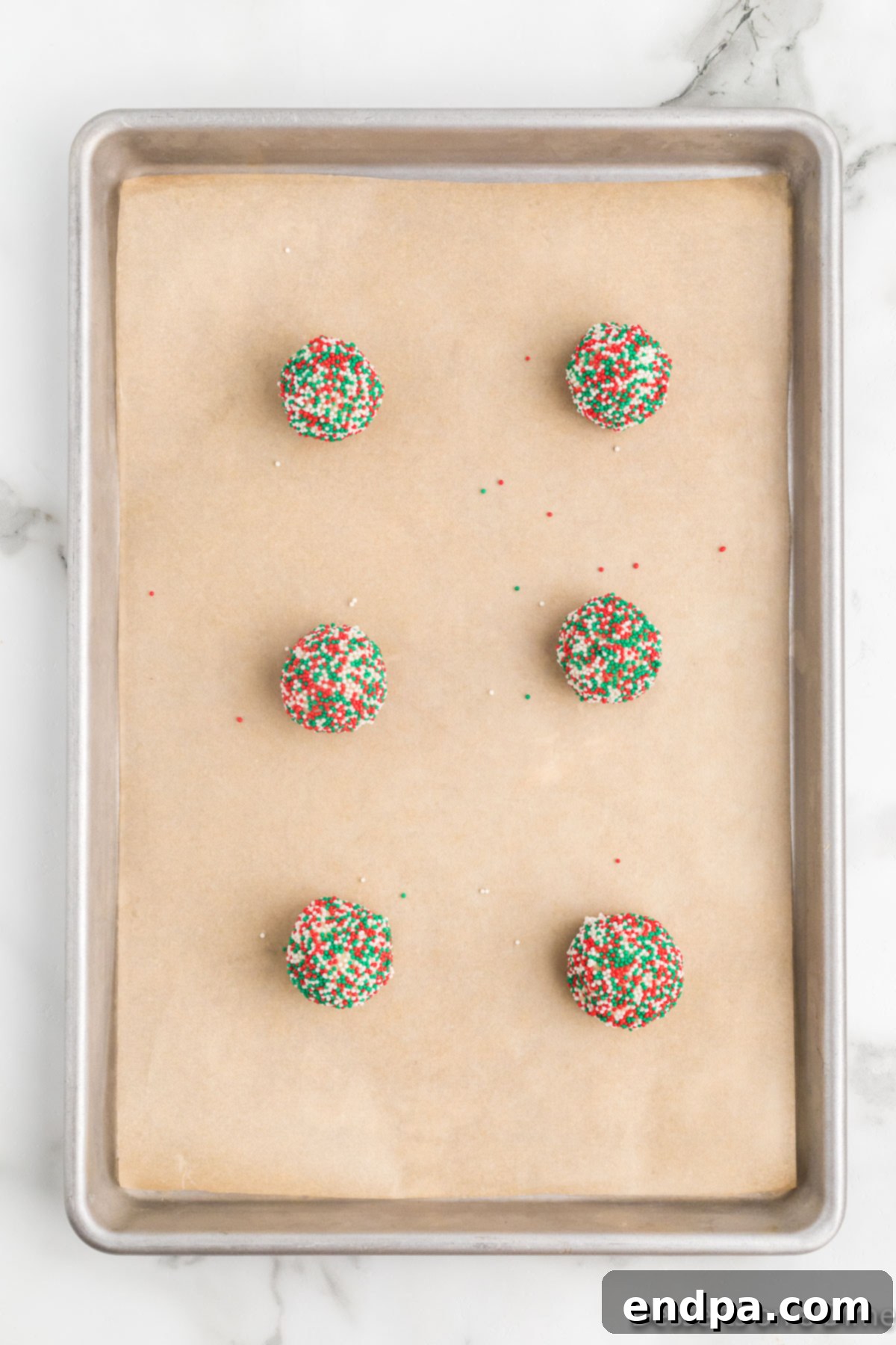 Several sprinkle-coated cookie dough balls neatly arranged and spaced on a parchment-lined baking sheet, ready for the oven.