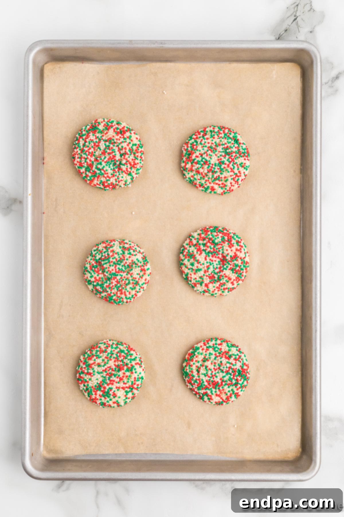 Freshly baked Christmas sprinkle cookies cooling on a baking sheet, showcasing their vibrant sprinkle coating and light golden edges.