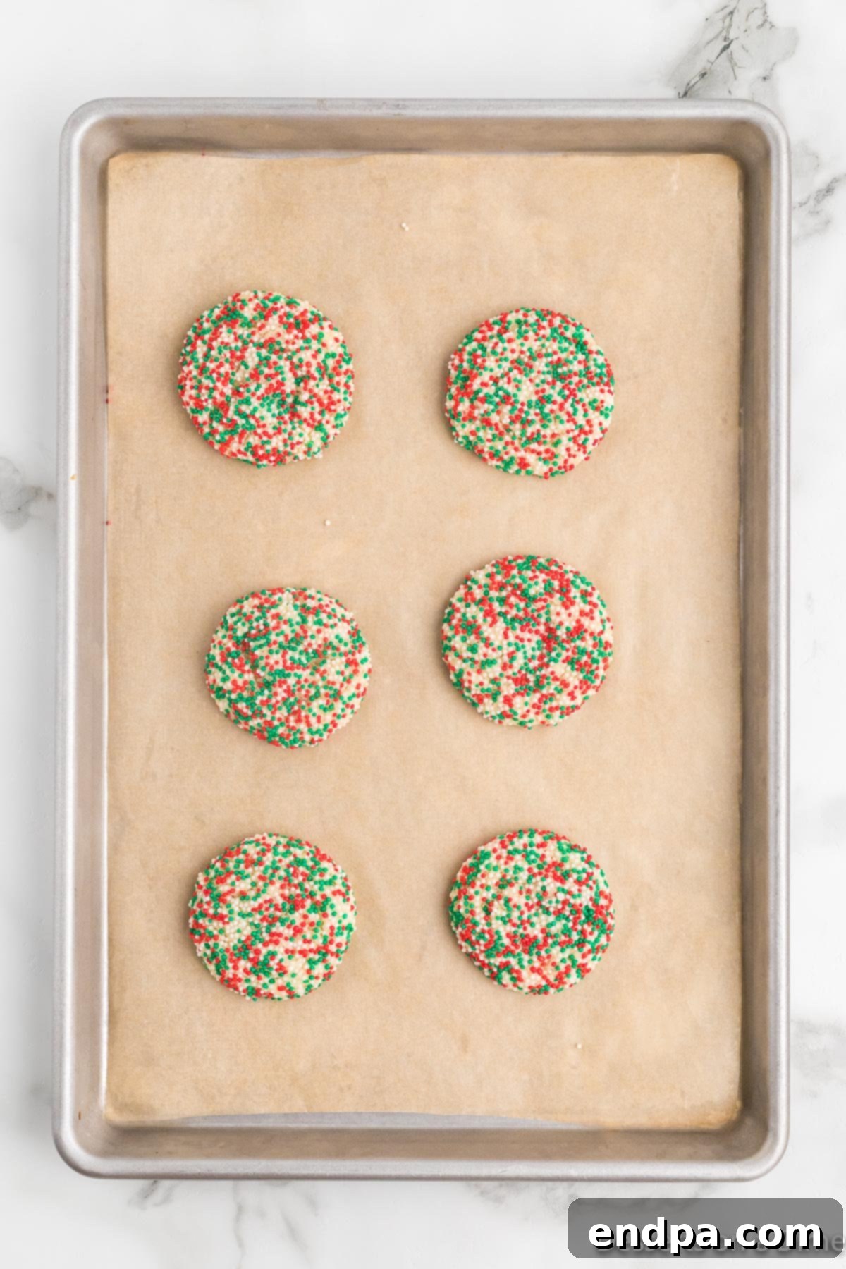 Baked Christmas sprinkle cookies resting on a baking sheet, allowing them to firm up before being transferred.