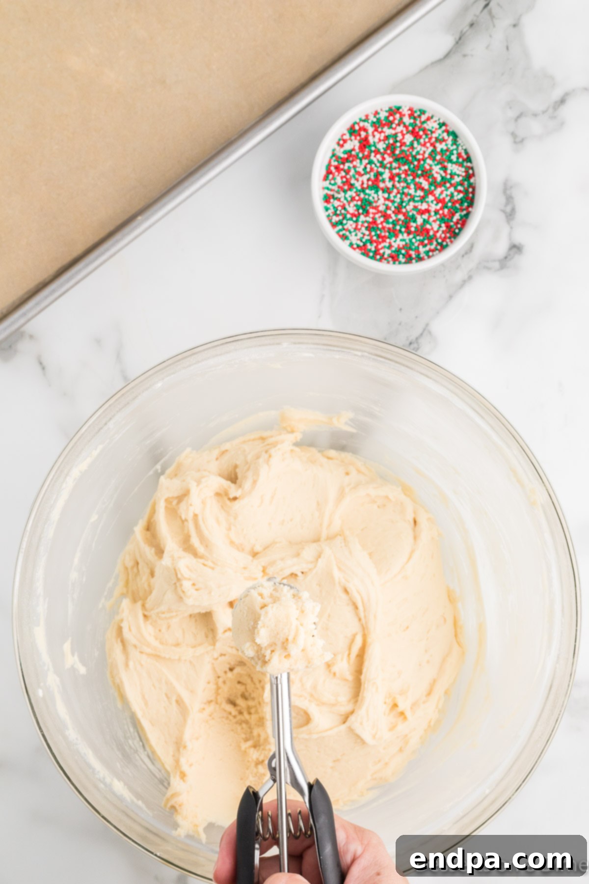 A cookie scoop gathering a consistent portion of chilled cookie dough from a mixing bowl.