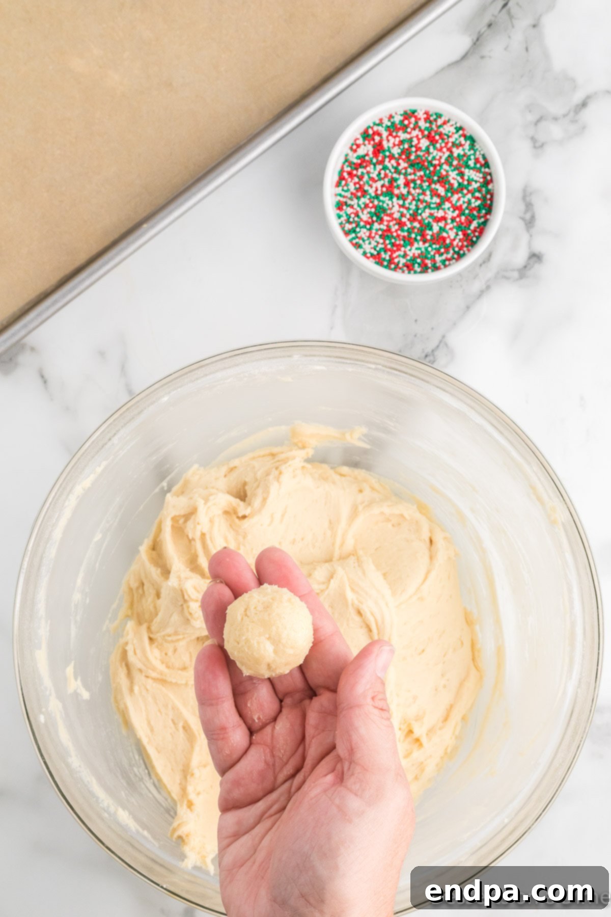 A perfectly formed, smooth ball of unbaked cookie dough gently held in a hand, showcasing its consistent shape.