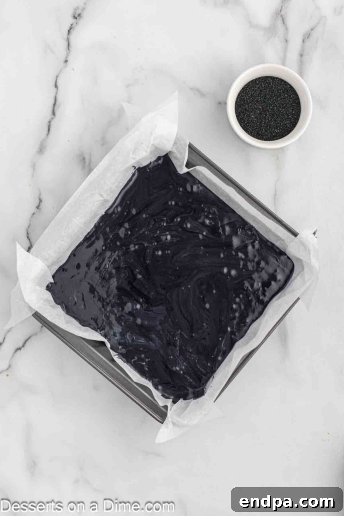 Naughty List Fudge 7 Black fudge mixture spread evenly into a baking dish lined with parchment paper, topped with sprinkles.