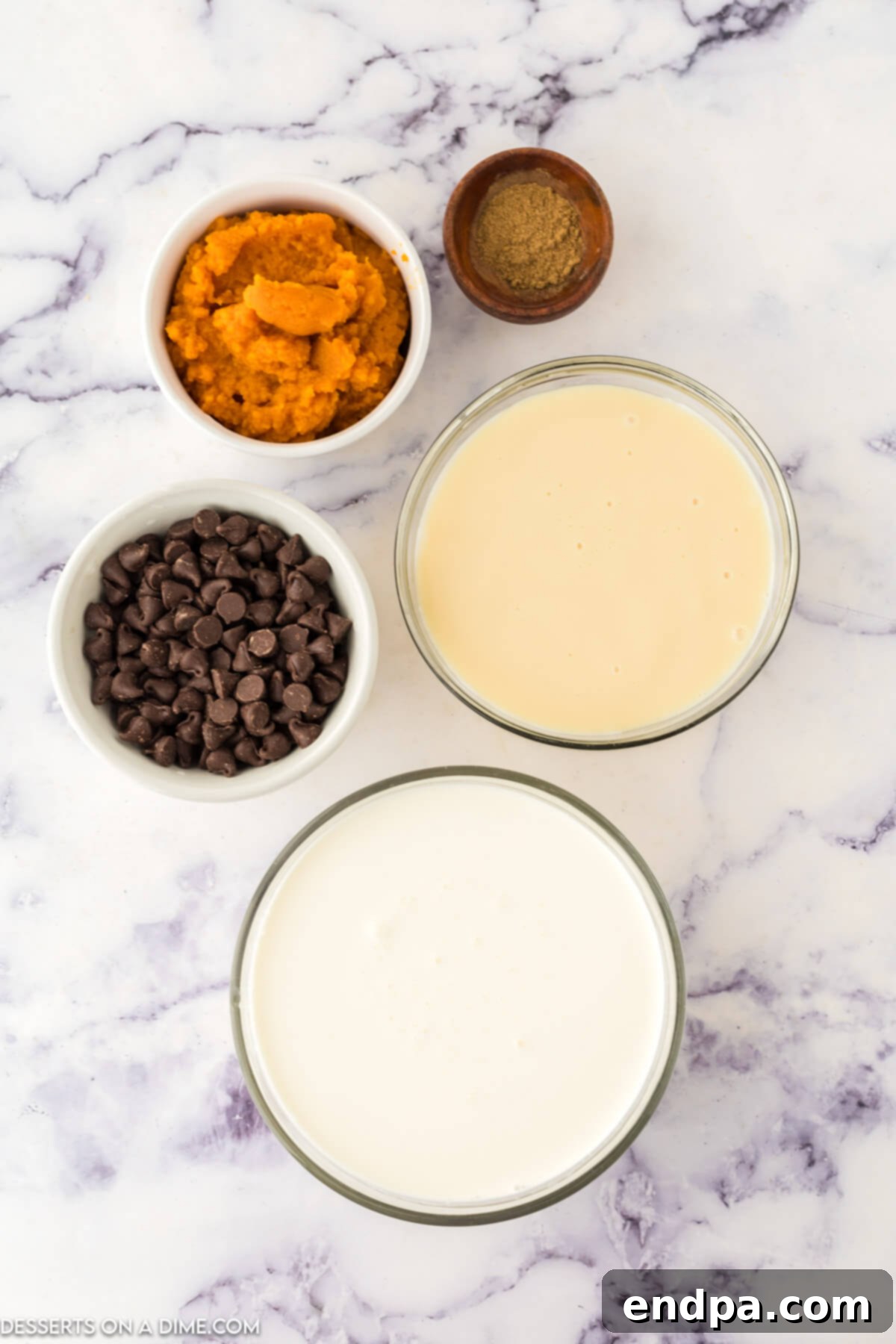 Heavy whipping cream, sweetened condensed milk, pumpkin puree, pumpkin pie spice, semi-sweet chocolate chips laid out on a wooden surface.