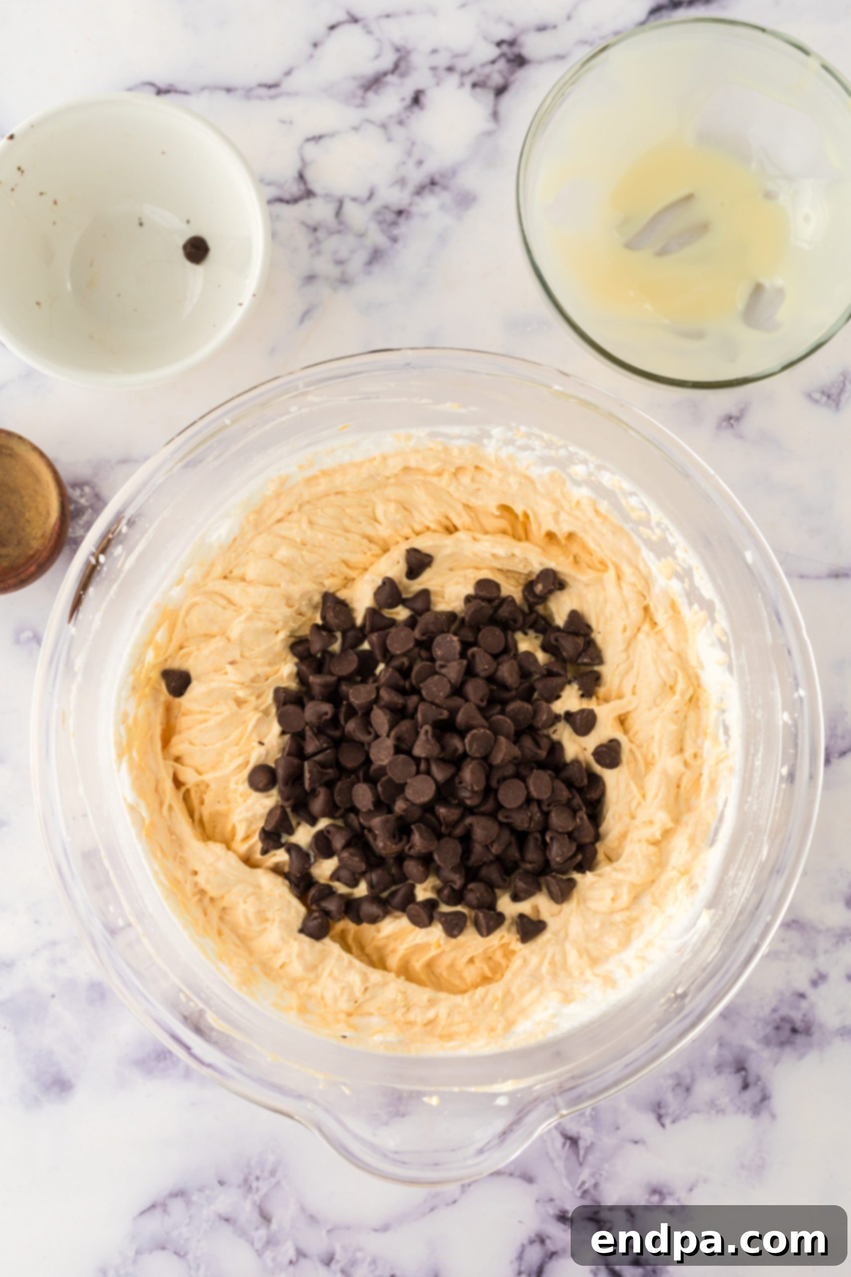Semi-sweet chocolate chips being folded into the pumpkin ice cream mixture with a spatula.