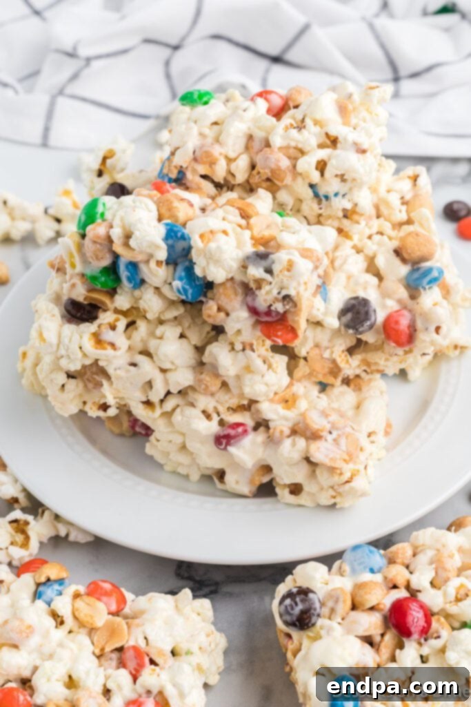 Popcorn Bars cut into neat squares, artfully stacked on a white plate, showcasing their colorful M&M's and peanut inclusions.