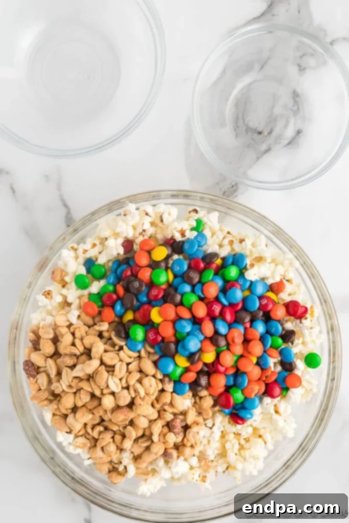 A large bowl filled with fluffy popcorn, crunchy peanuts, and colorful M&M's, perfectly mixed and ready for the marshmallow coating.