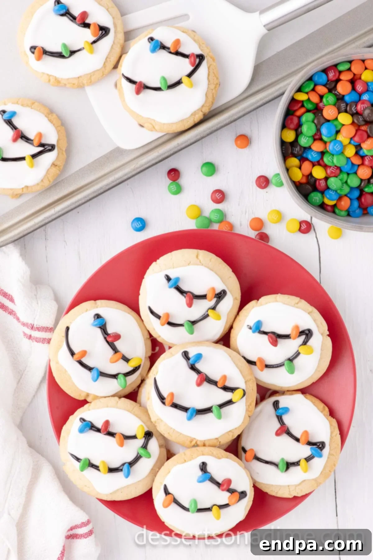 A vibrant stack of Christmas Light Cookies, showcasing their colorful M&M 'lights' and intricate black gel 'strings', arranged on a festive red platter.