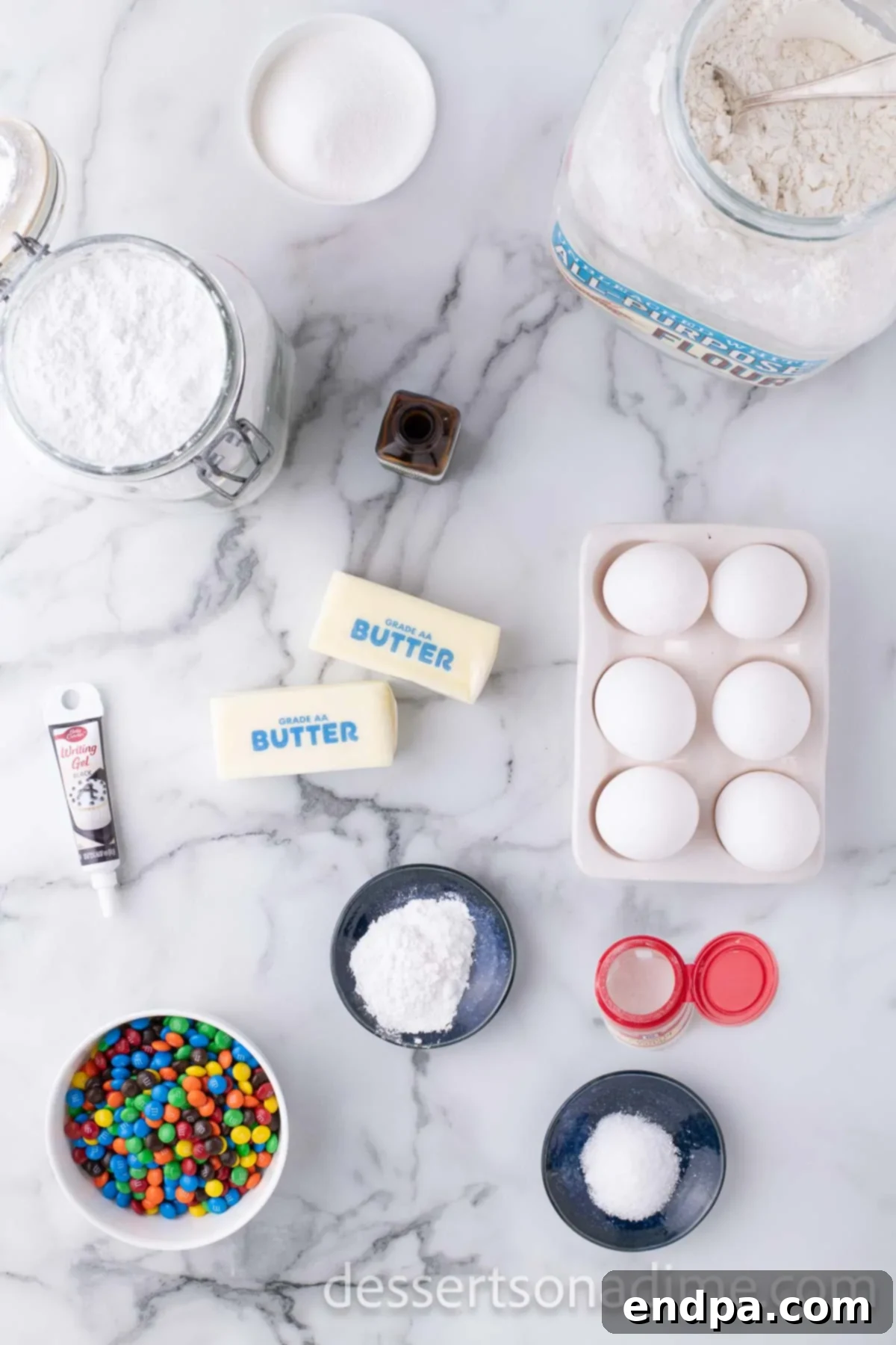 A flat lay of ingredients for Christmas Light Cookies including flour, softened butter, vanilla extract, eggs, powdered sugar, cream of tartar, black writing gel, and mini M&M's.