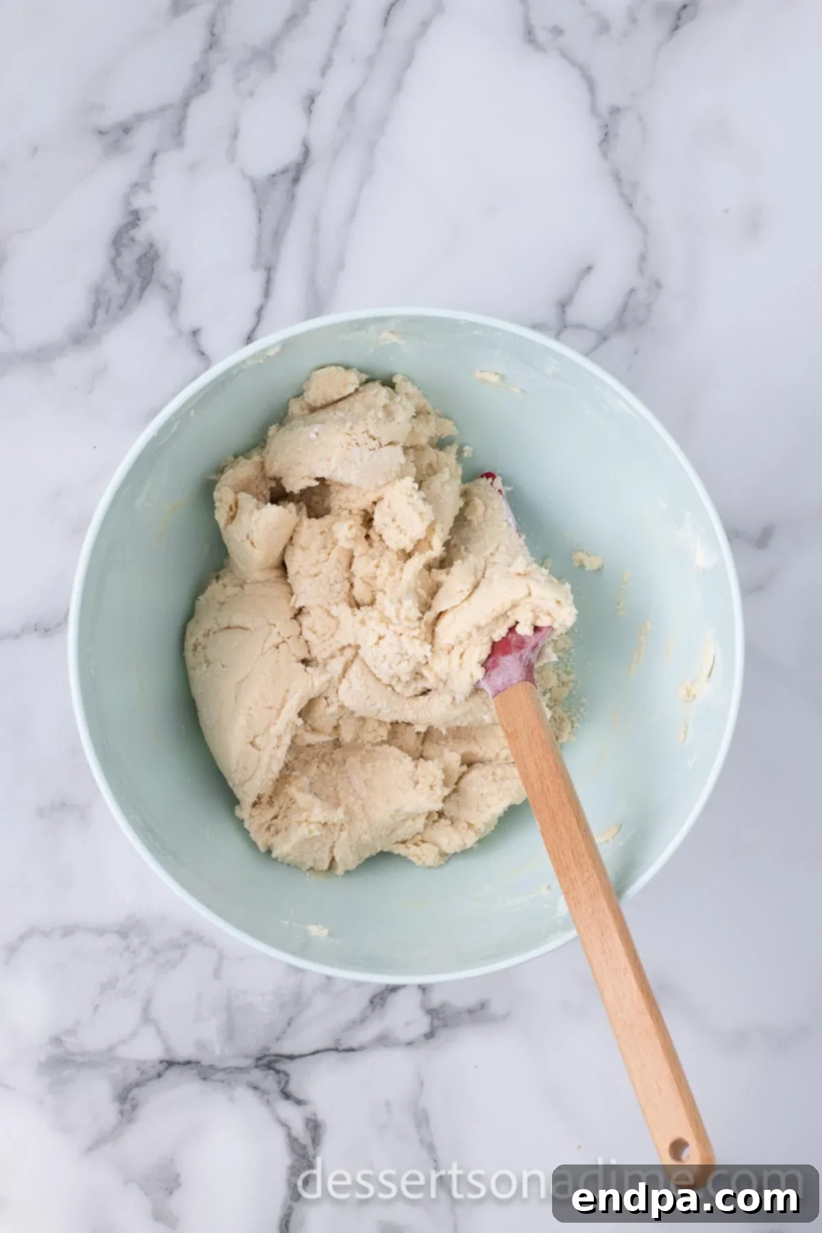The cookie dough is fully combined in the mixing bowl, with a spatula resting in the smooth, coherent dough.