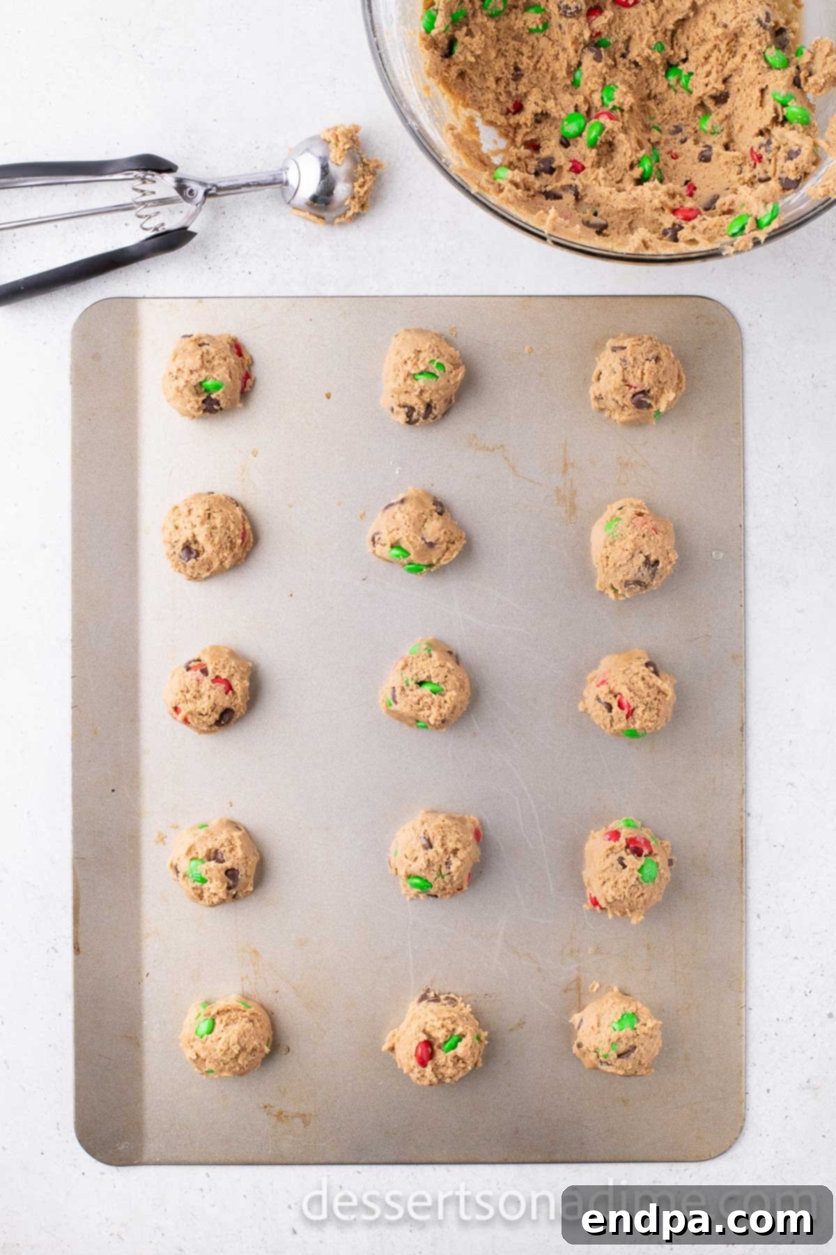 Scooped cookie dough balls topped with extra M&M's arranged on a parchment-lined baking sheet, ready for baking.