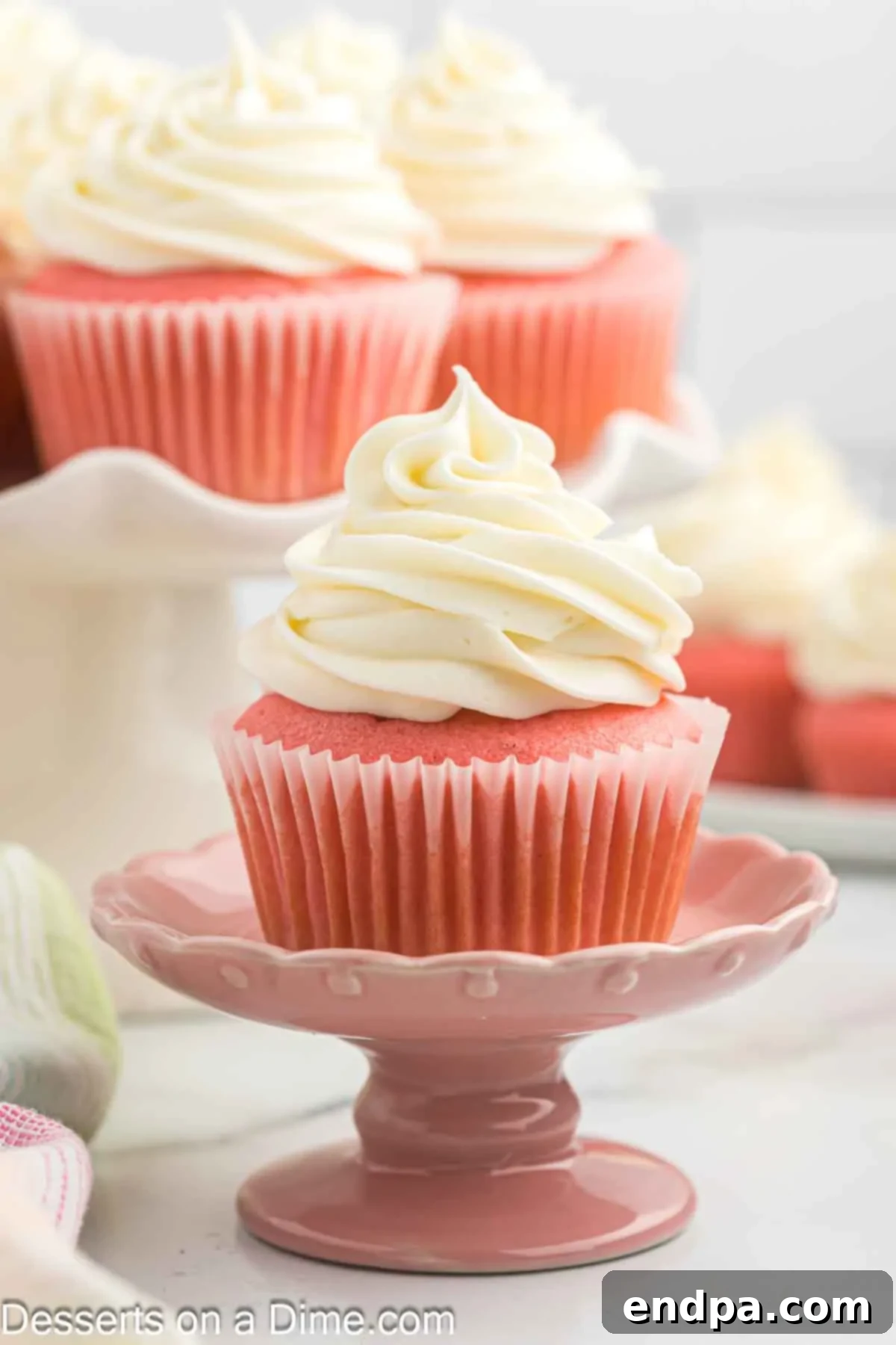 A beautifully decorated Pink Velvet Cupcake with cream cheese frosting, elegantly presented on a white pedestal.