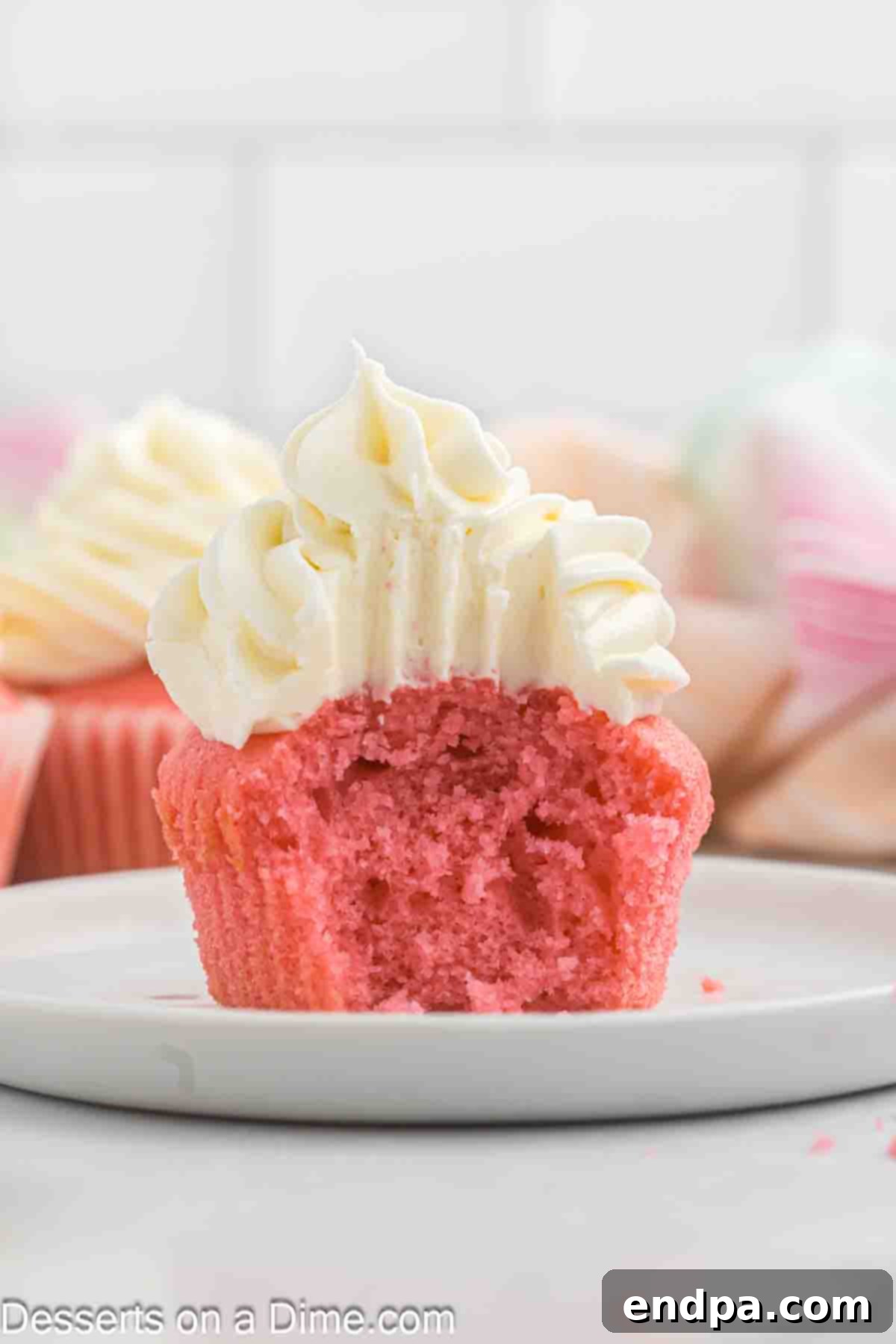 A pink velvet cupcake, frosted and cut in half, revealing its moist pink interior.