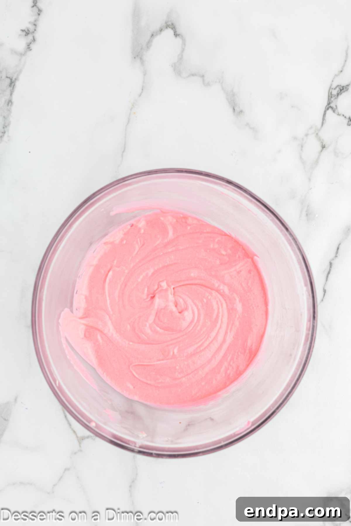Pink food coloring being added drop by drop to the cupcake batter in a mixing bowl.
